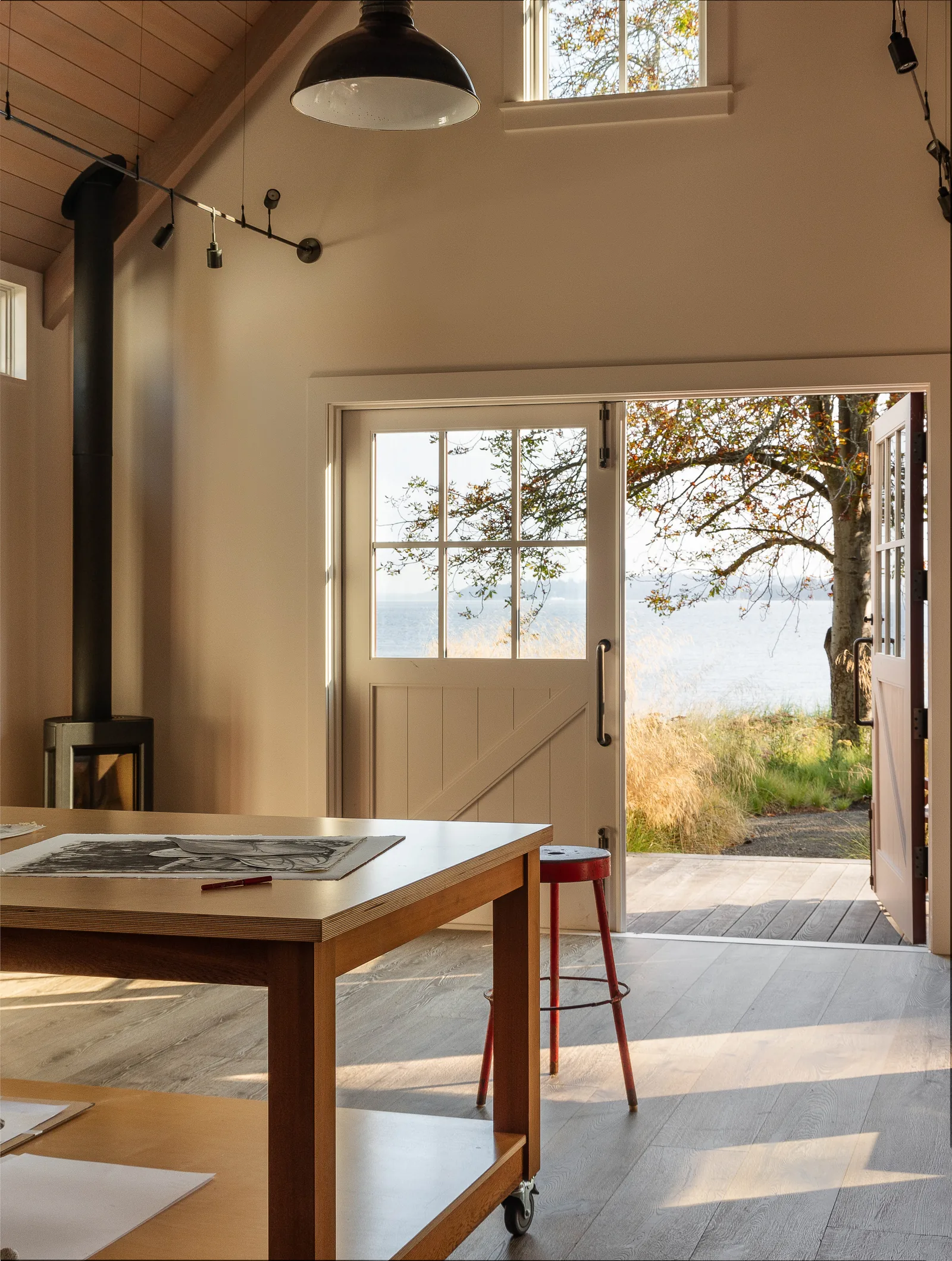 Room with vaulted ceiling features double Dutch doors opening to a deck with a waterfront view.