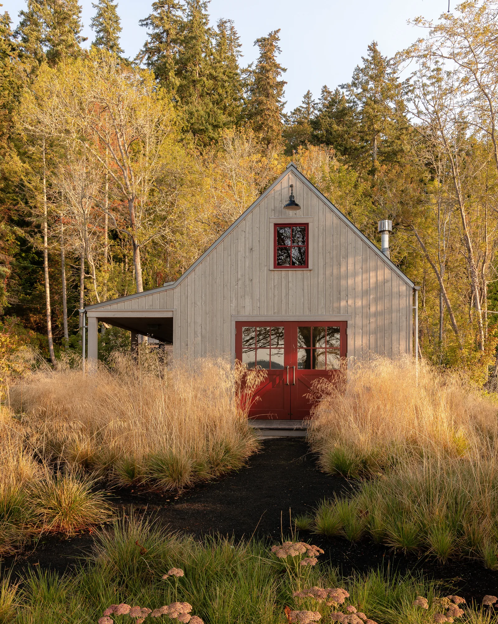 Small wooden house with gable roof, red framed windows and doors, located in a natural landscape with tall grasses.
