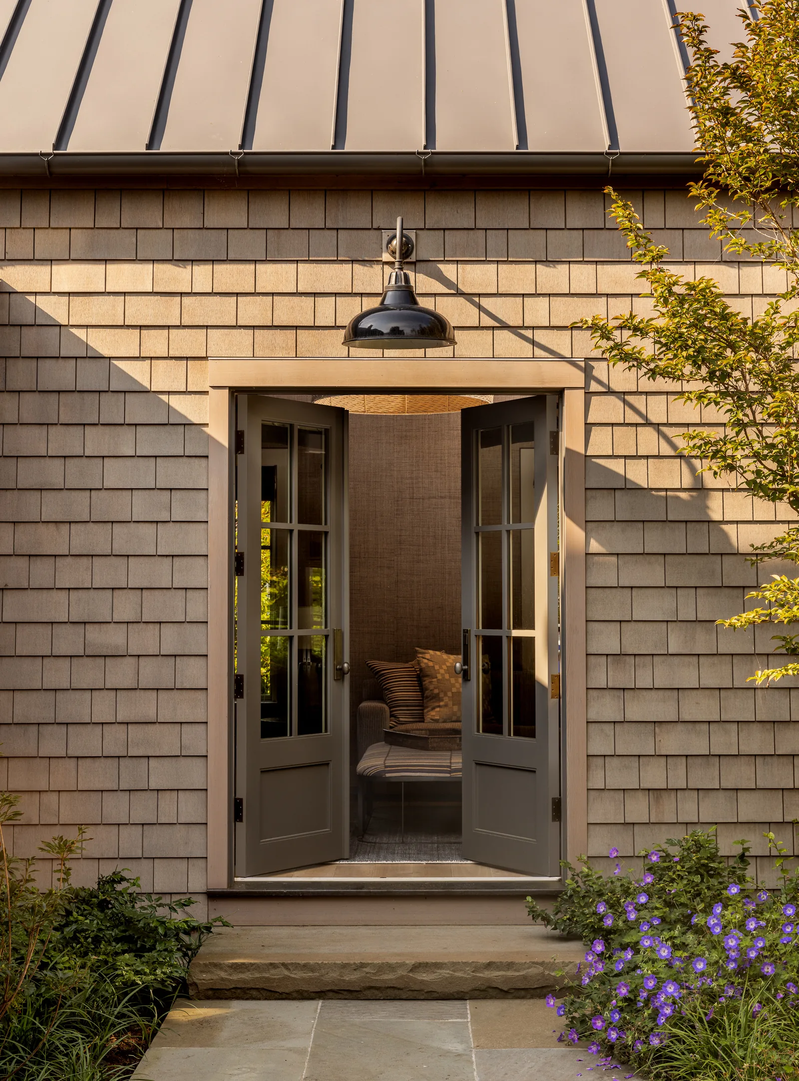 Rear exterior of a shingle-style building with open French doors and a metal roof above.