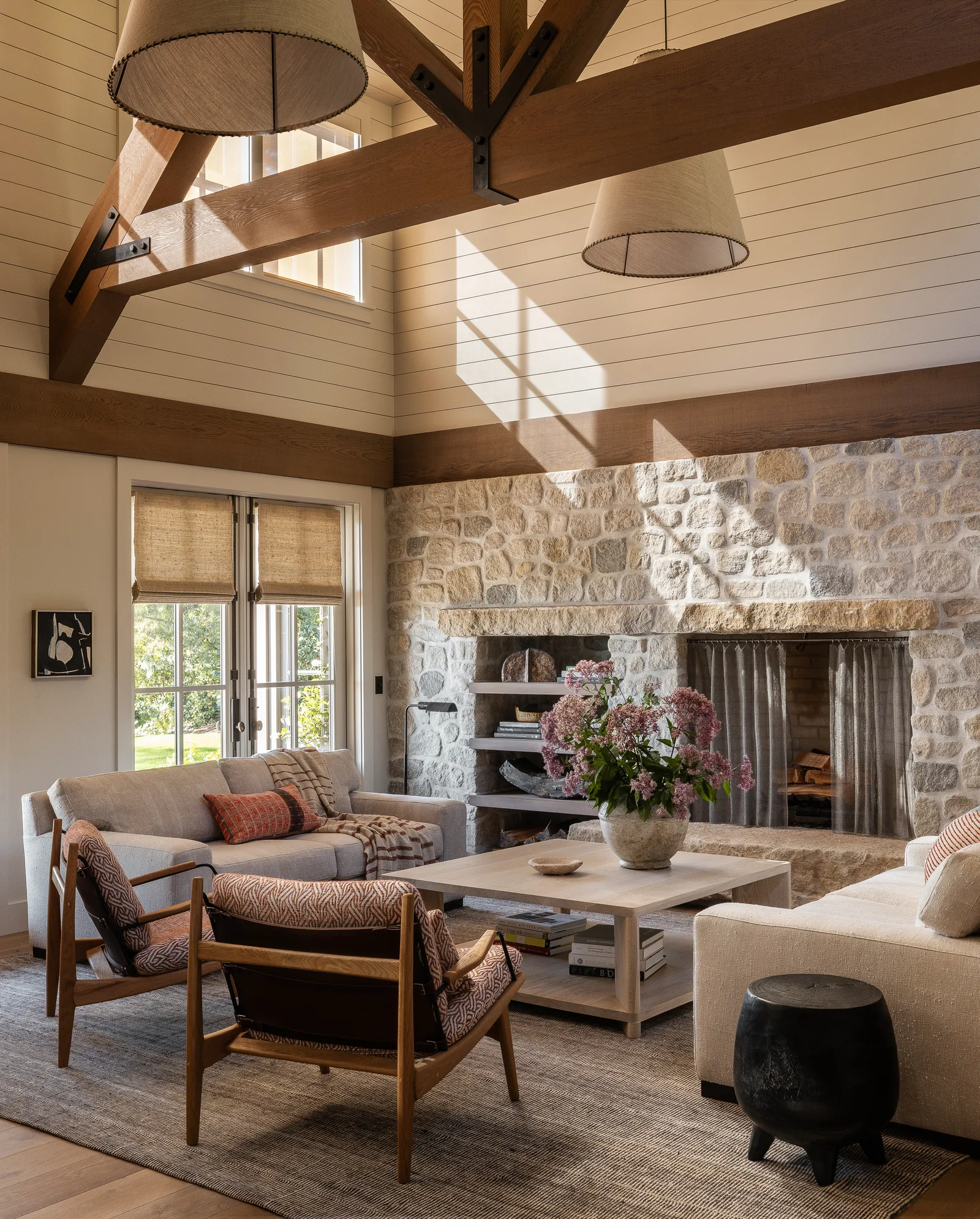 Living room featuring a stone fireplace wall, exposed wood beam ceiling, and a seating area with sofas and armchairs.