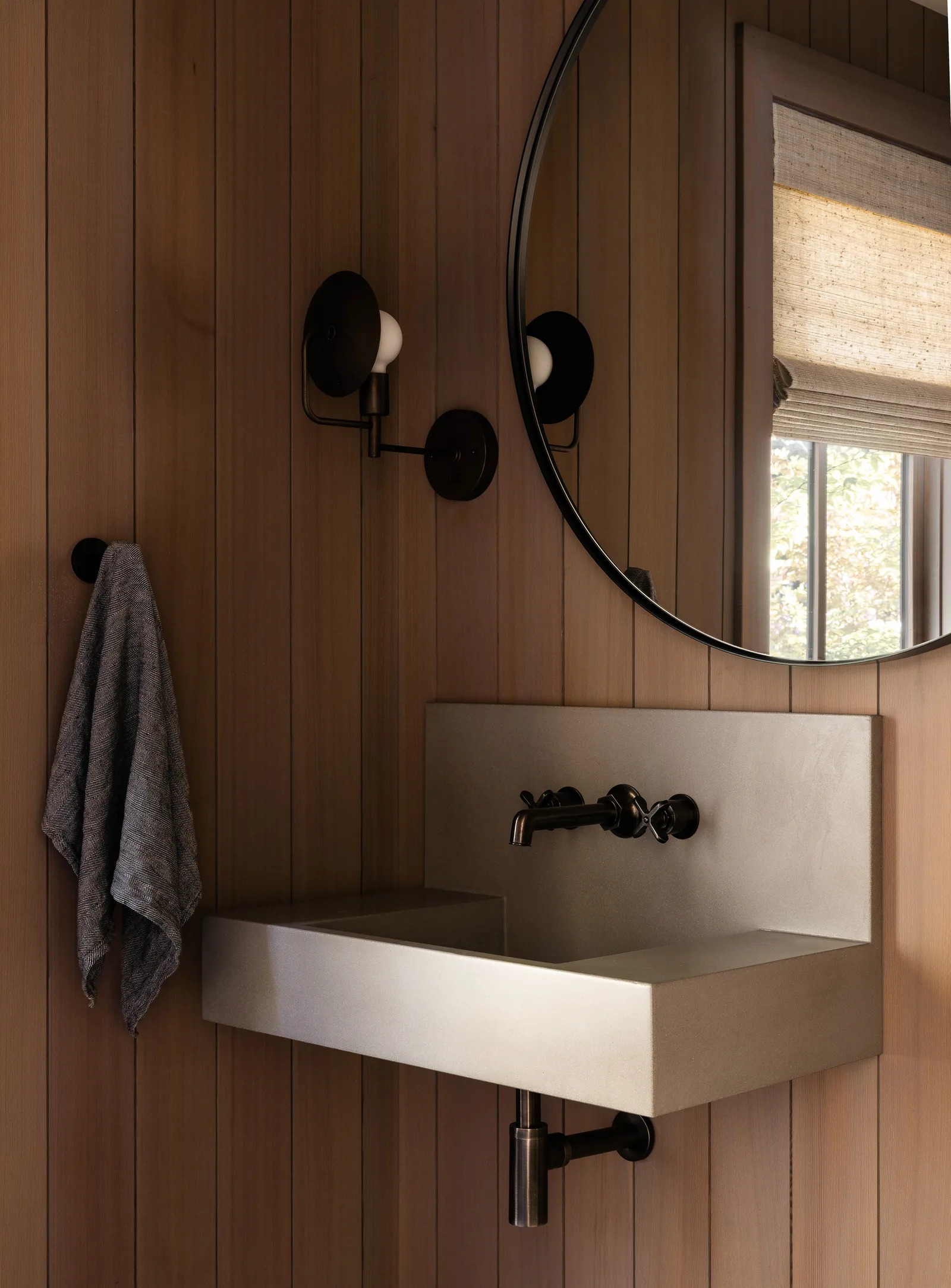 Wall-mounted sink and faucet with a round mirror and wood panel walls in a bathroom.
