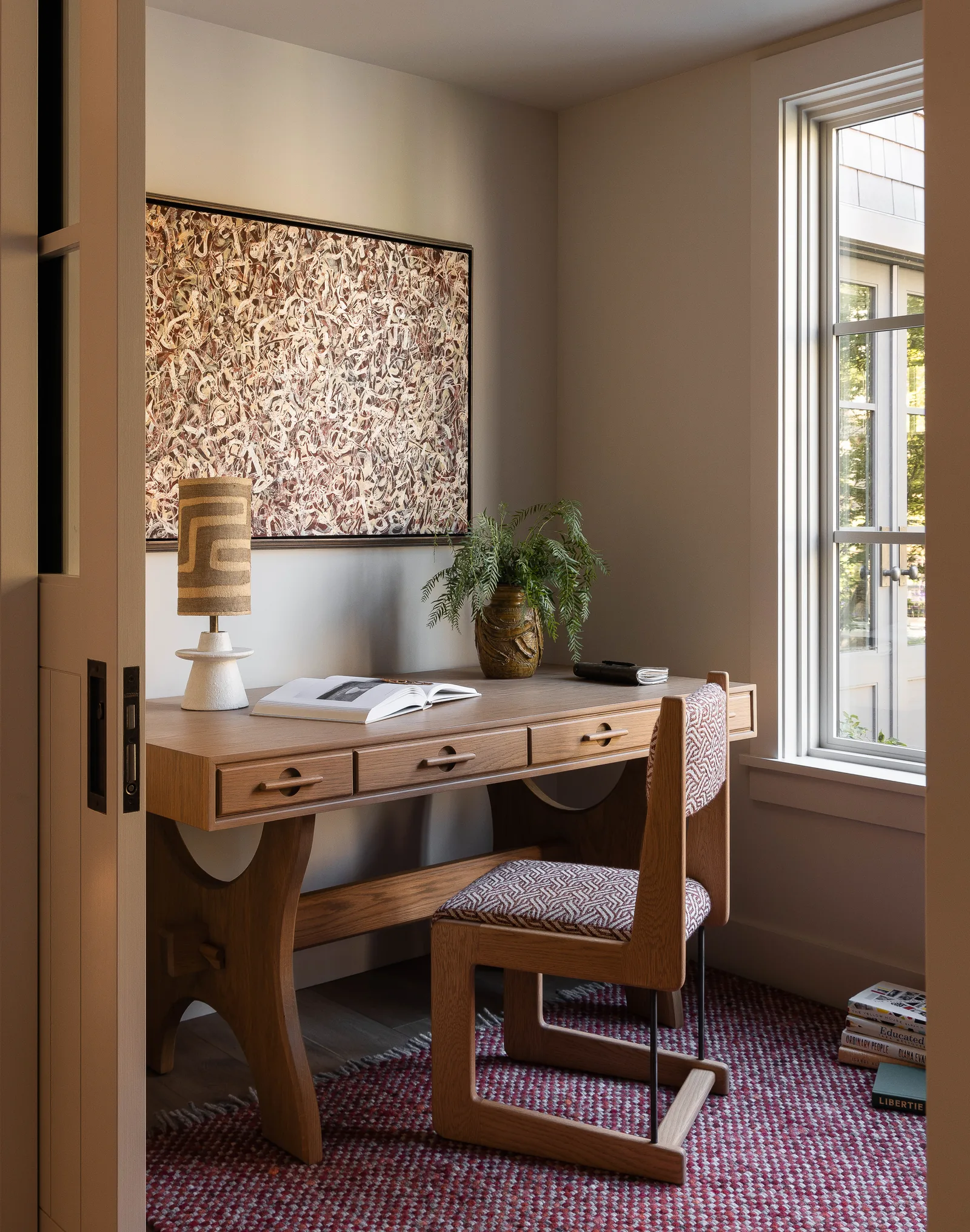 Home office with wooden desk and chair positioned beside a large window with natural light.