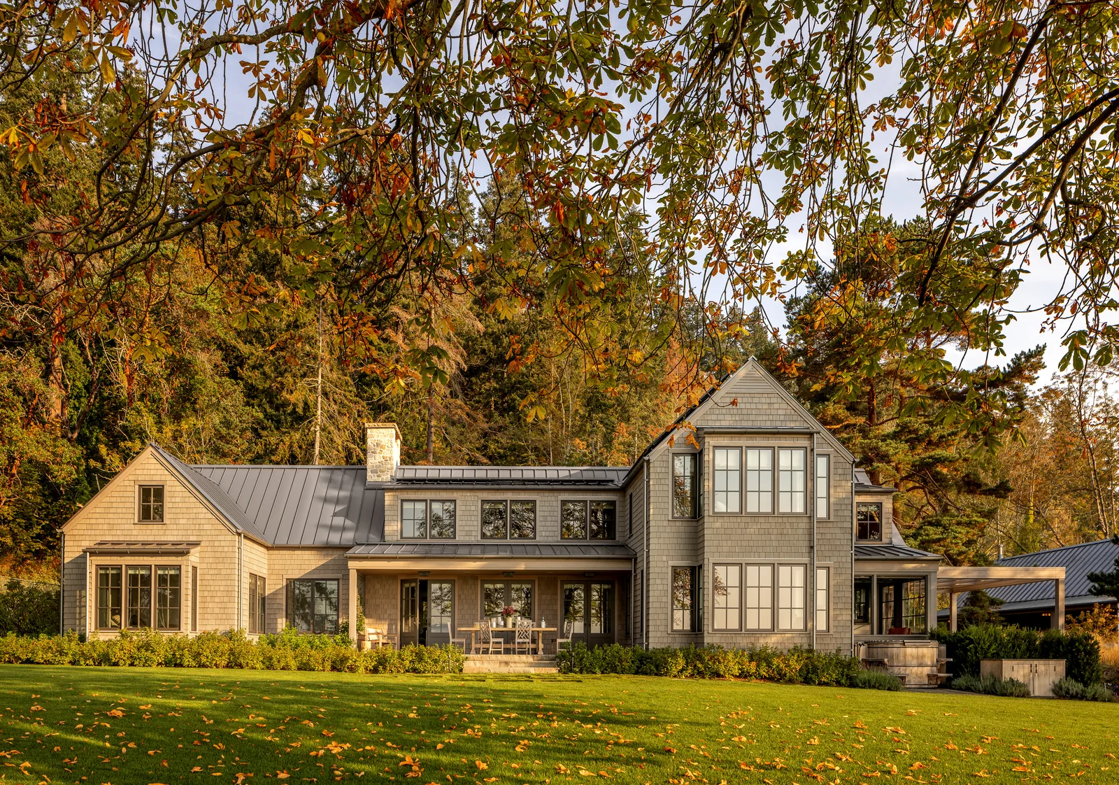 Two-story residential house with gray shingle siding and metal roofing, featuring large windows and a front porch.
