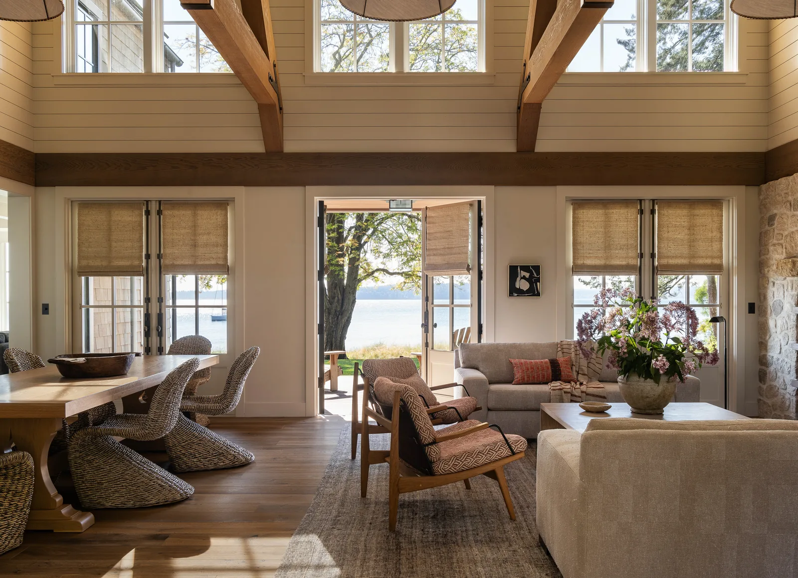 Interior view showing wood beams, large glazed doors, and a seating area overlooking a water landscape.
