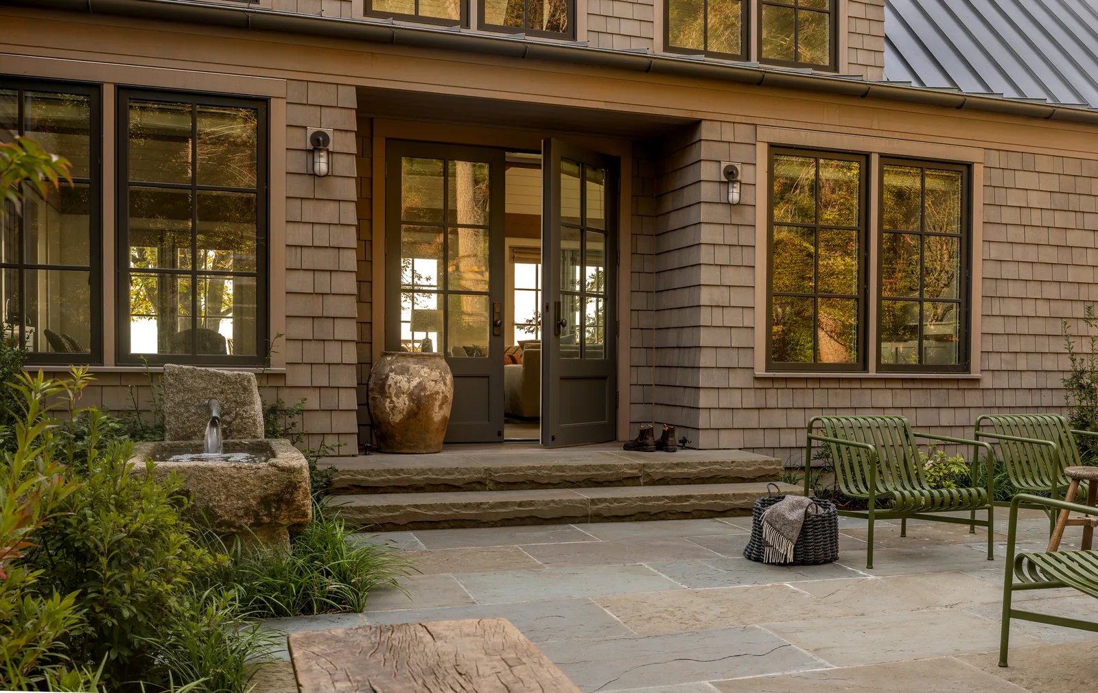 Exterior rear view of a house showing a stone patio with seating and a water feature.