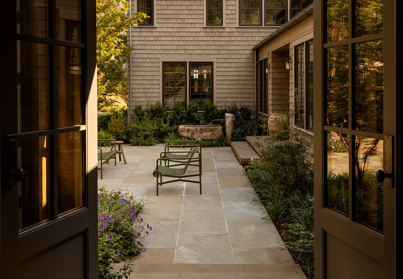 Stone courtyard with metal seating and landscaping enclosed by a shingle-sided residence.