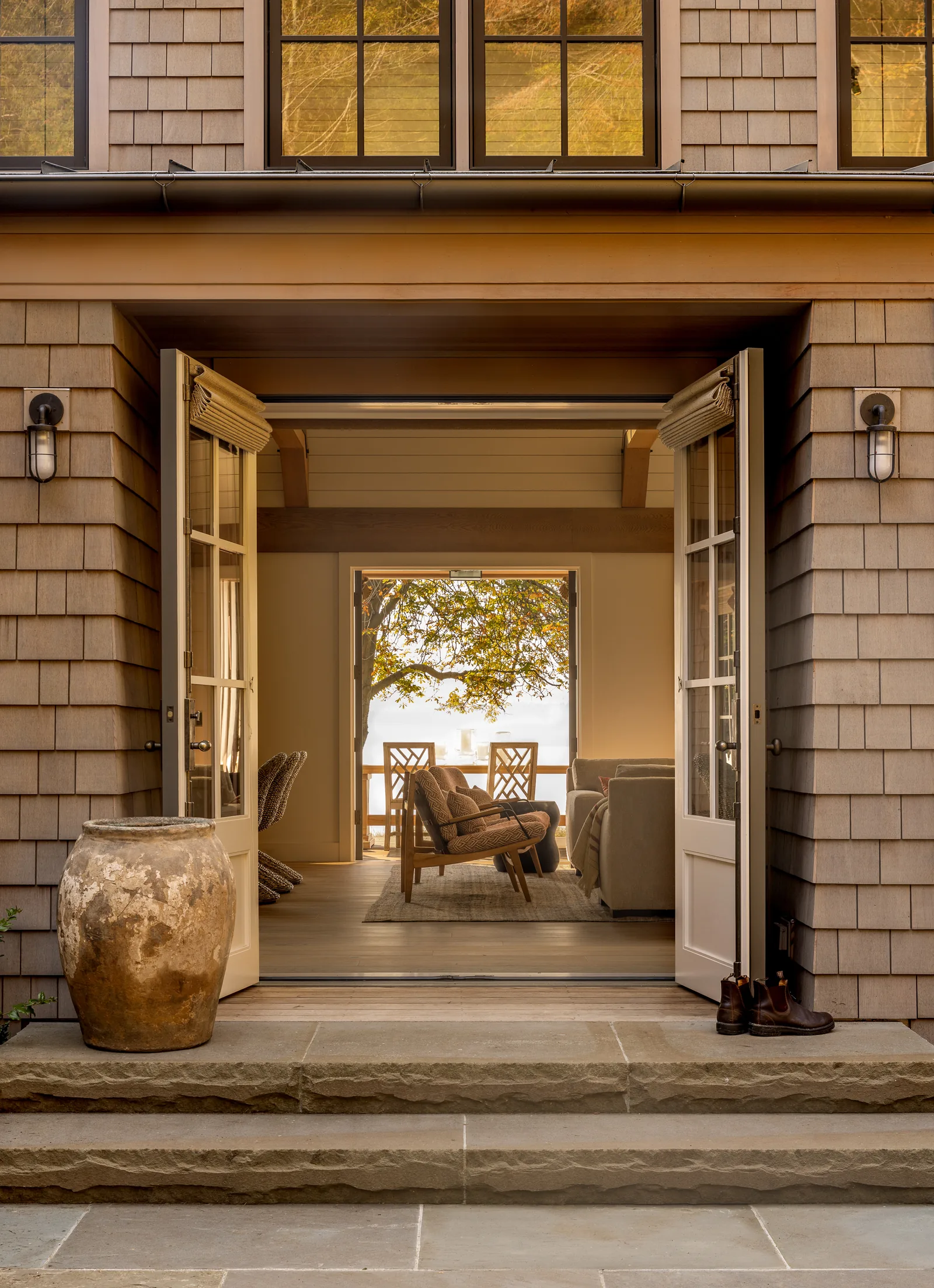Exterior view through open double doors into a living and dining area with views of a tree and water beyond.