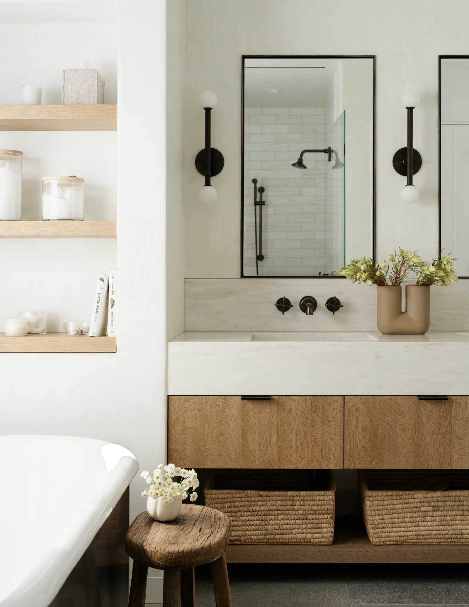 Bathroom interior with floating wooden vanity, dual mirrors, wall sconces, and freestanding bathtub.