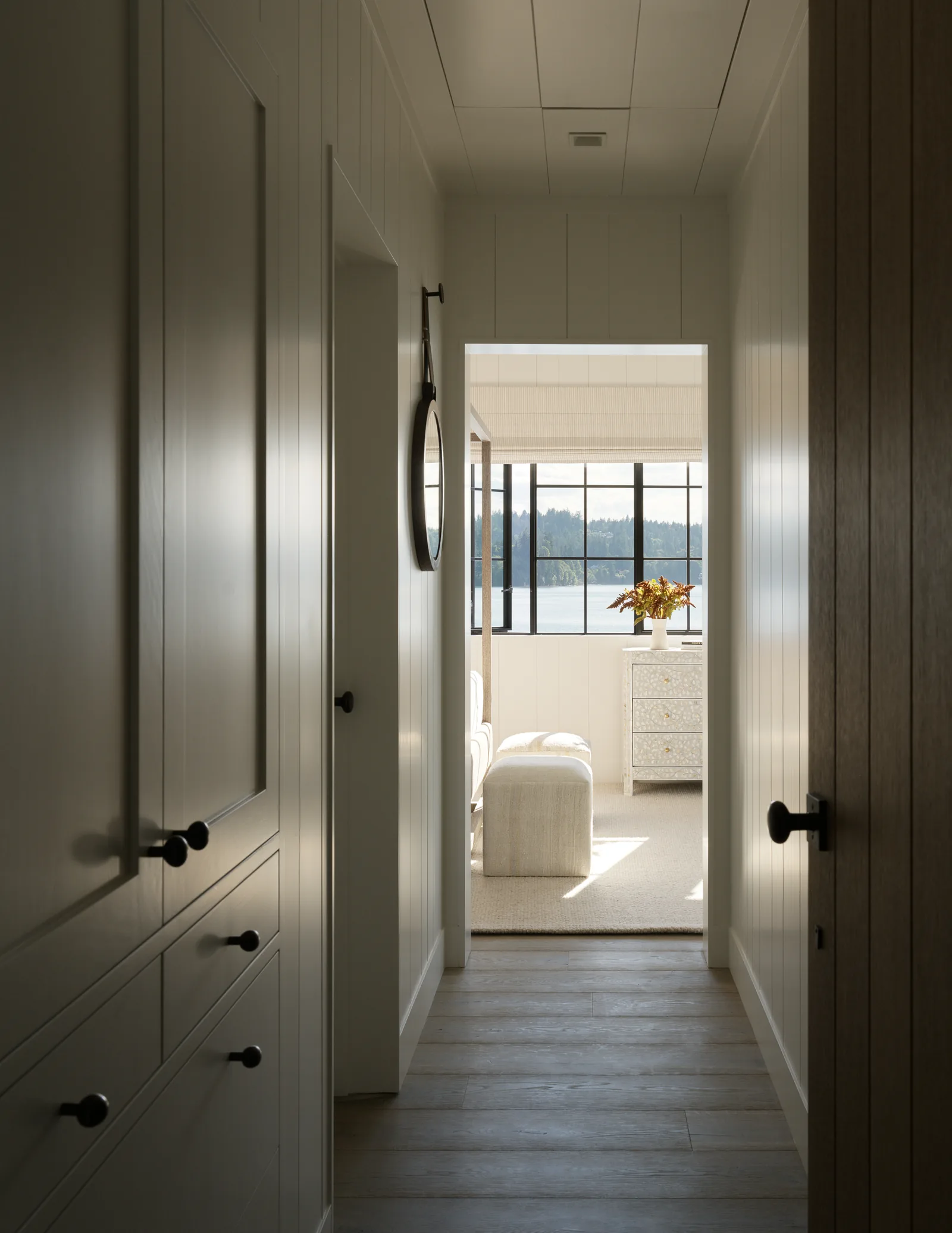 Narrow hallway leads to a light-filled room with large steel-framed windows offering water views.