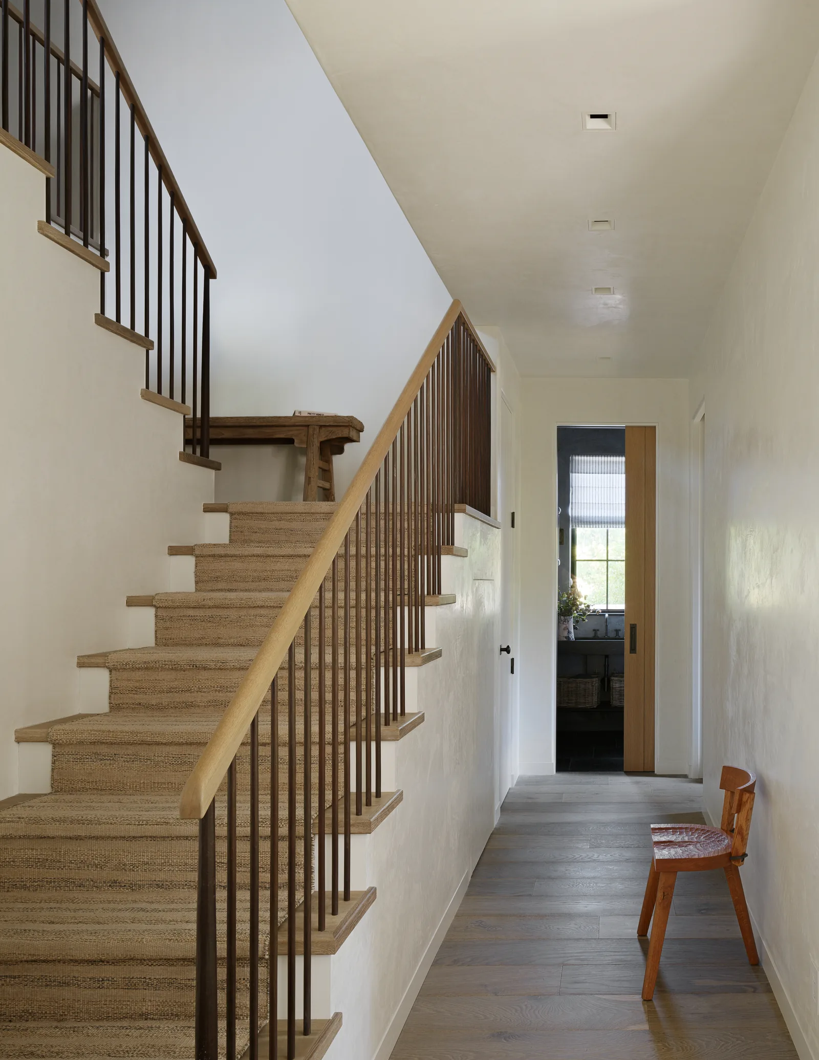 Interior hallway featuring carpeted stairs with wooden railing and a wooden chair along the wall.