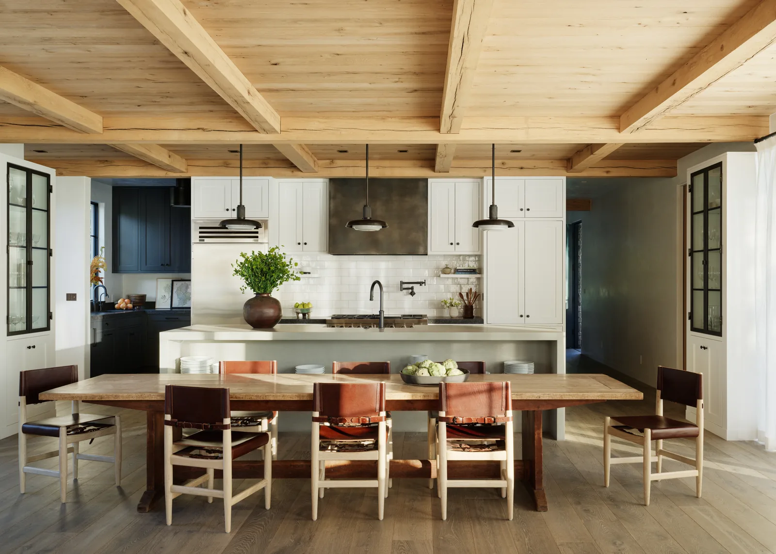 View of dining area and kitchen with wood ceiling beams, white cabinets, and center island.