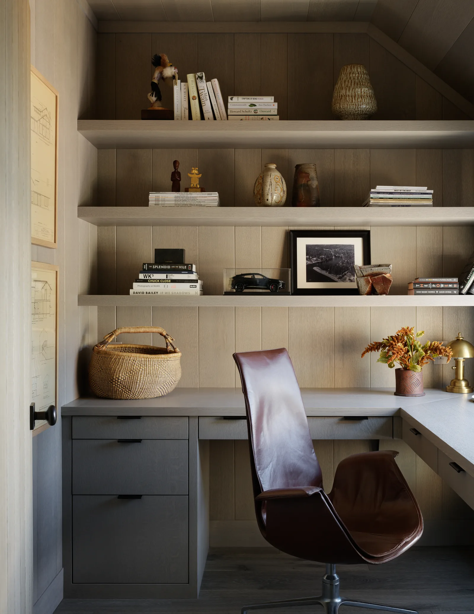 Built-in corner desk and open shelving in a home office with wood panel walls and a leather chair.