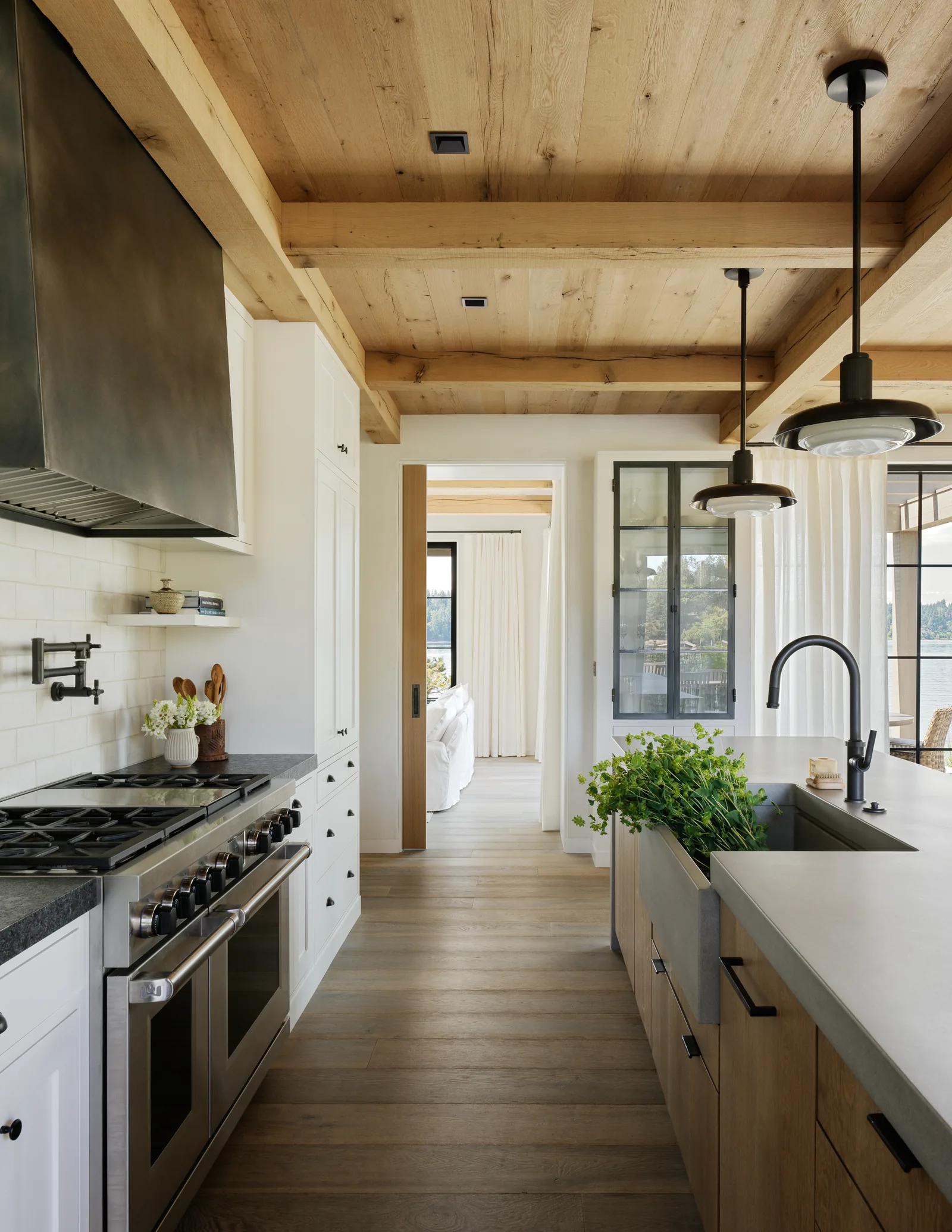 Kitchen with wooden ceiling beams, white cabinetry, stainless steel range, and large island with sink and pendant lights.