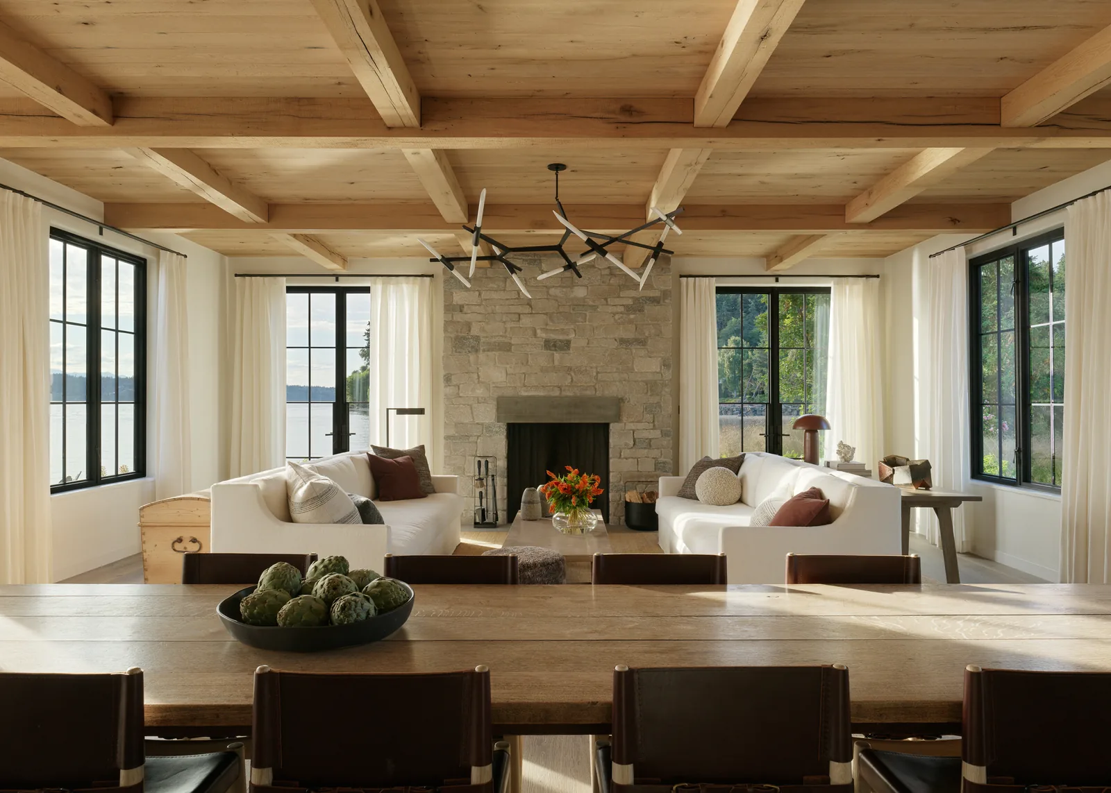 Living room features a wooden coffered ceiling and stone fireplace flanked by large windows with white curtains.