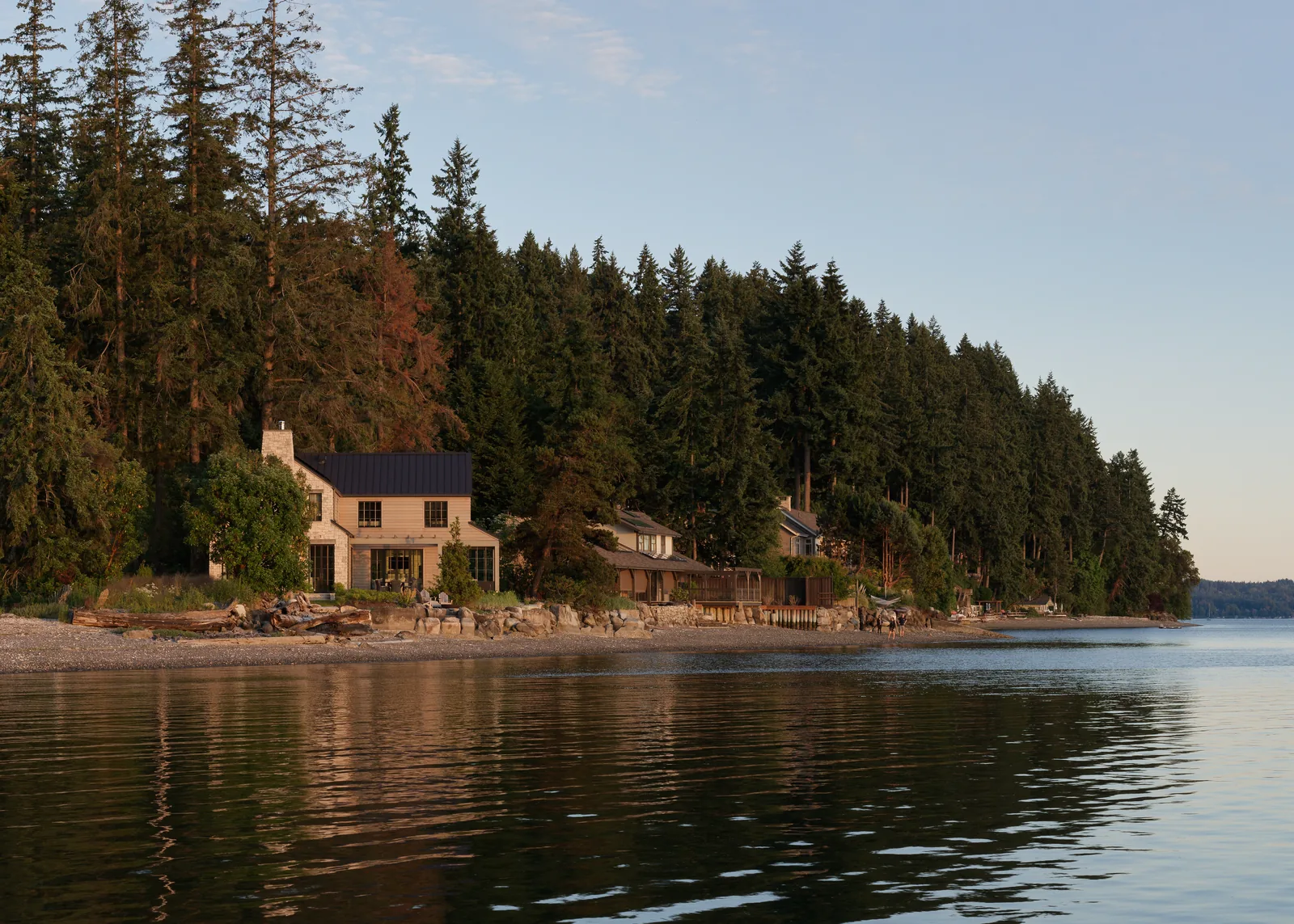 Two-story residential house on a forested shoreline with calm water in front at Arrow Bay project.