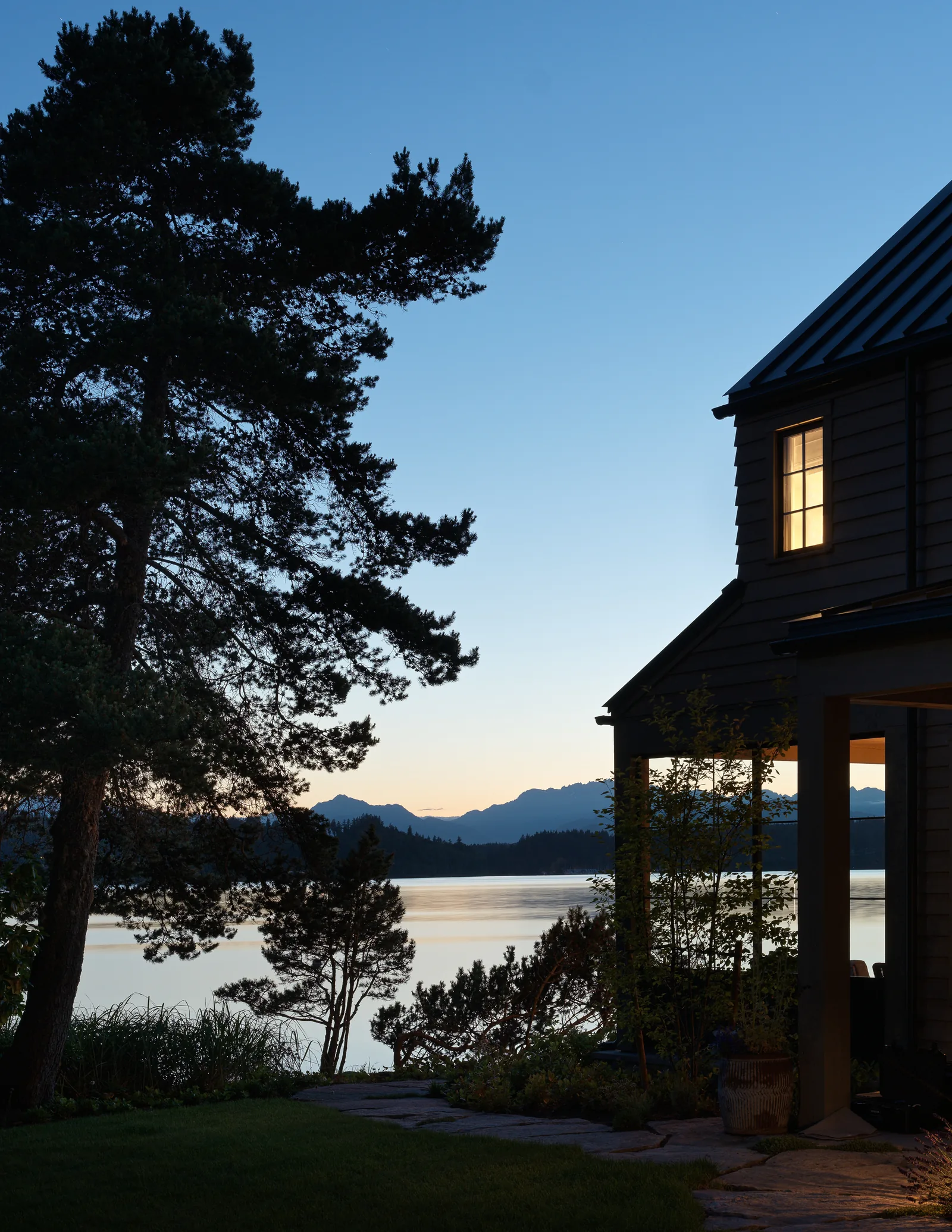 Lakeside home exterior at dusk featuring natural landscaping and silhouetted trees.
