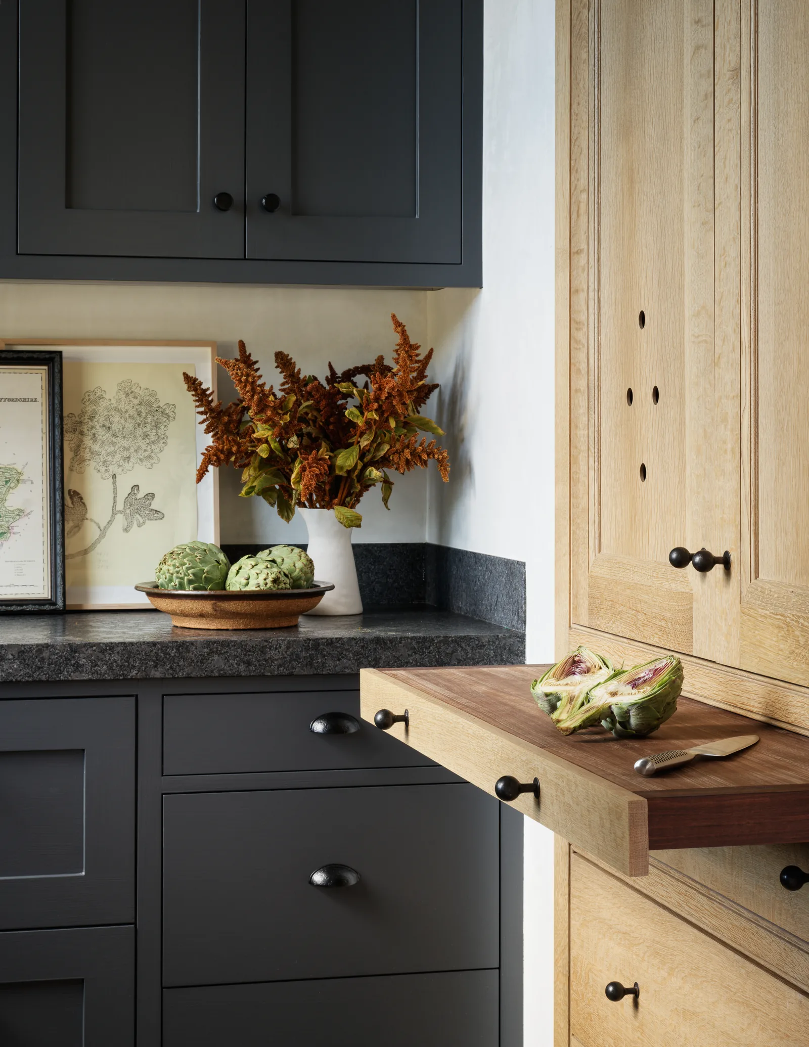 Kitchen cabinetry featuring dark gray cabinets with black granite countertops and light wood with a pull-out cutting board.