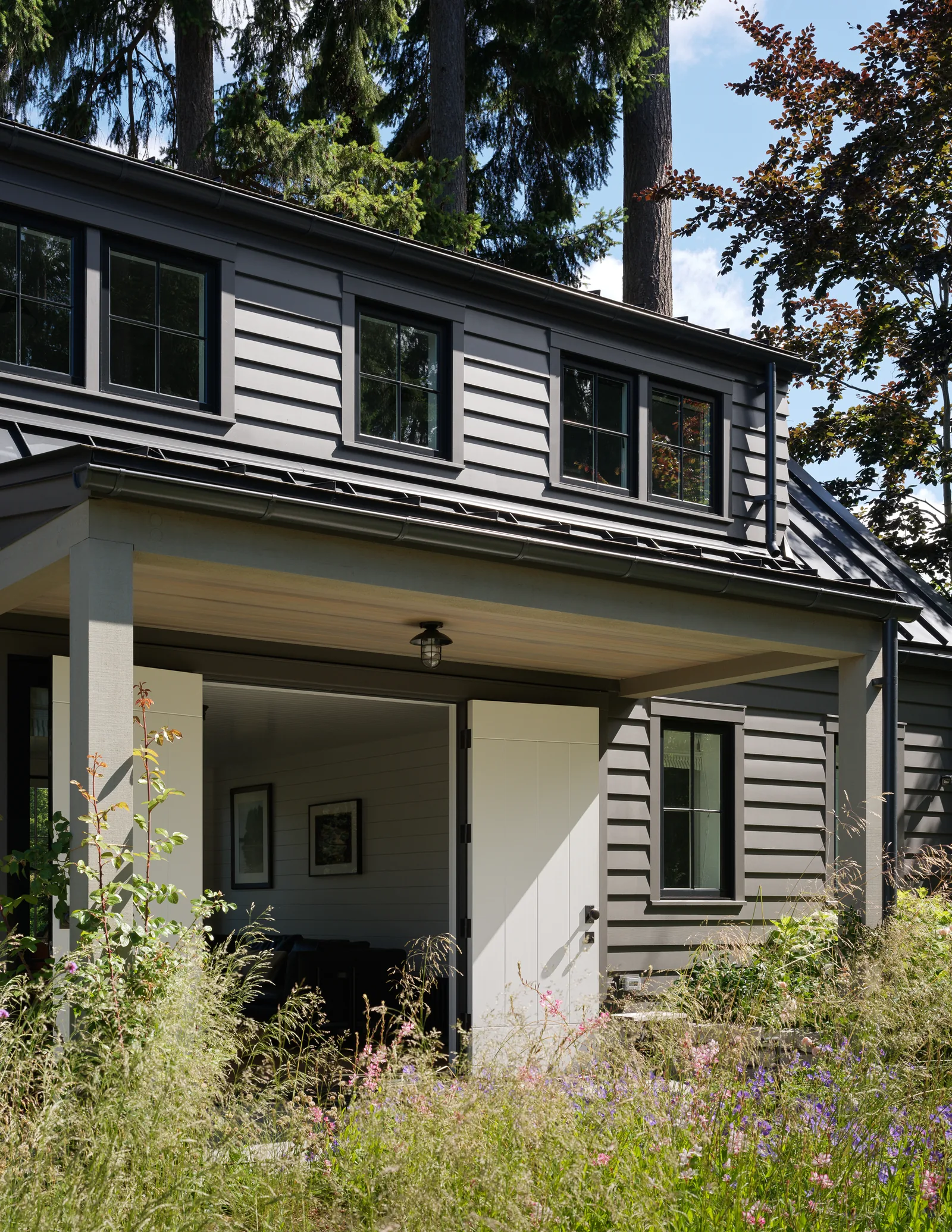 Covered porch with open white double doors and windows on upper and lower floors of a gray siding house.