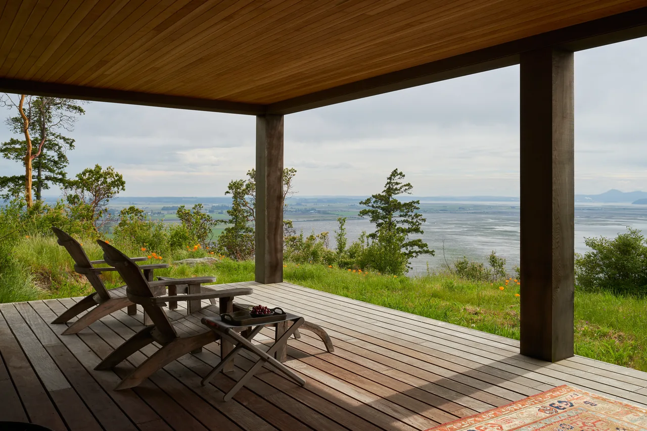 Covered deck with Adirondack chairs offers views of a river valley and distant hills from Chuckanut Studio.
