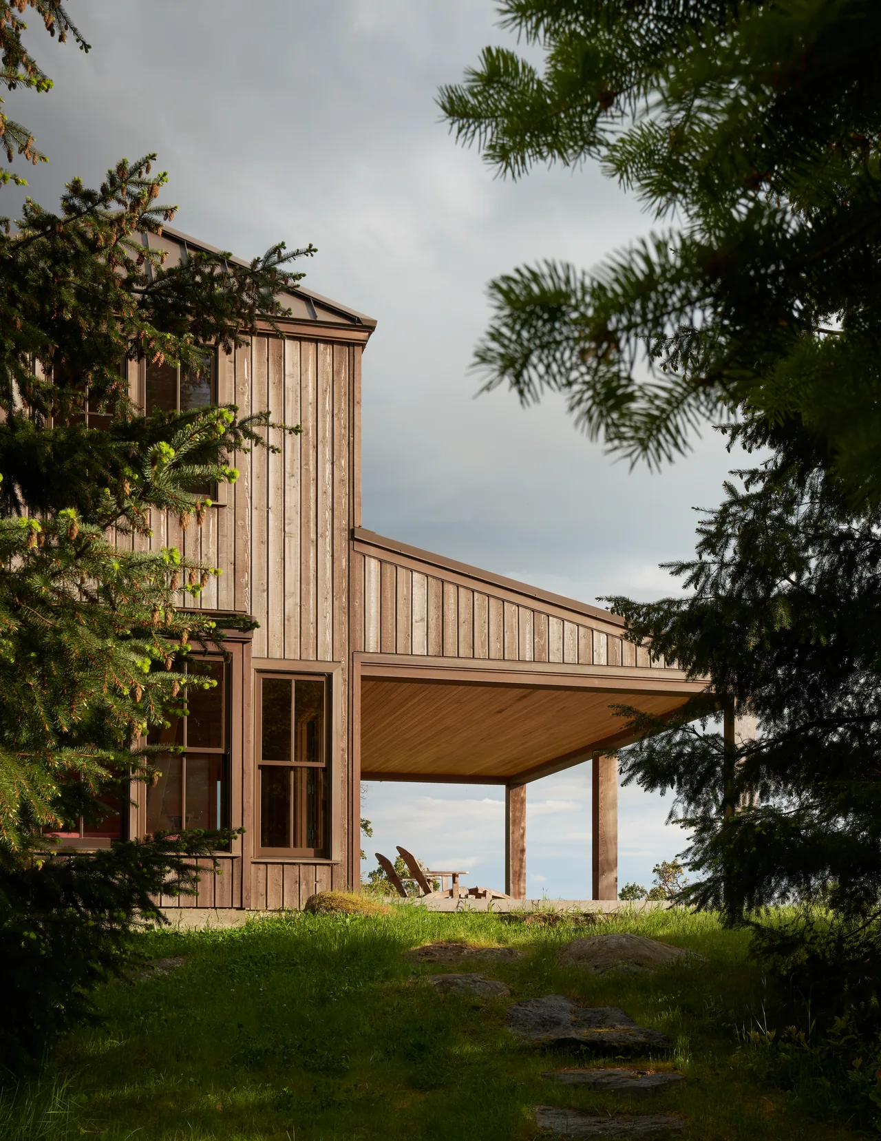 Chuckanut Studio features vertical wood siding and a covered outdoor patio nestled among trees on a grassy hilltop.