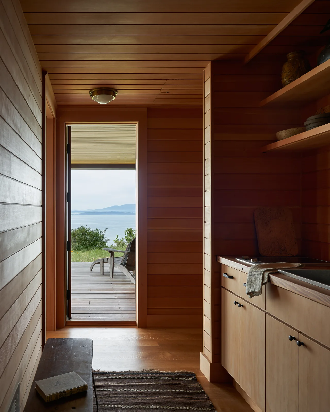 Wood-paneled hallway opens to a deck with seating and a view of water and mountains beyond.