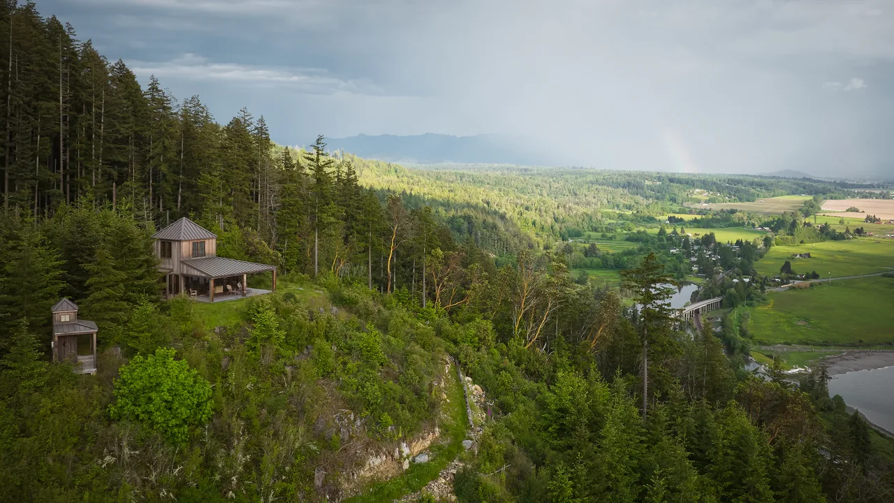 Chuckanut Studio on a forested hillside with covered porch and metal roof, overlooking a river valley and farmland.