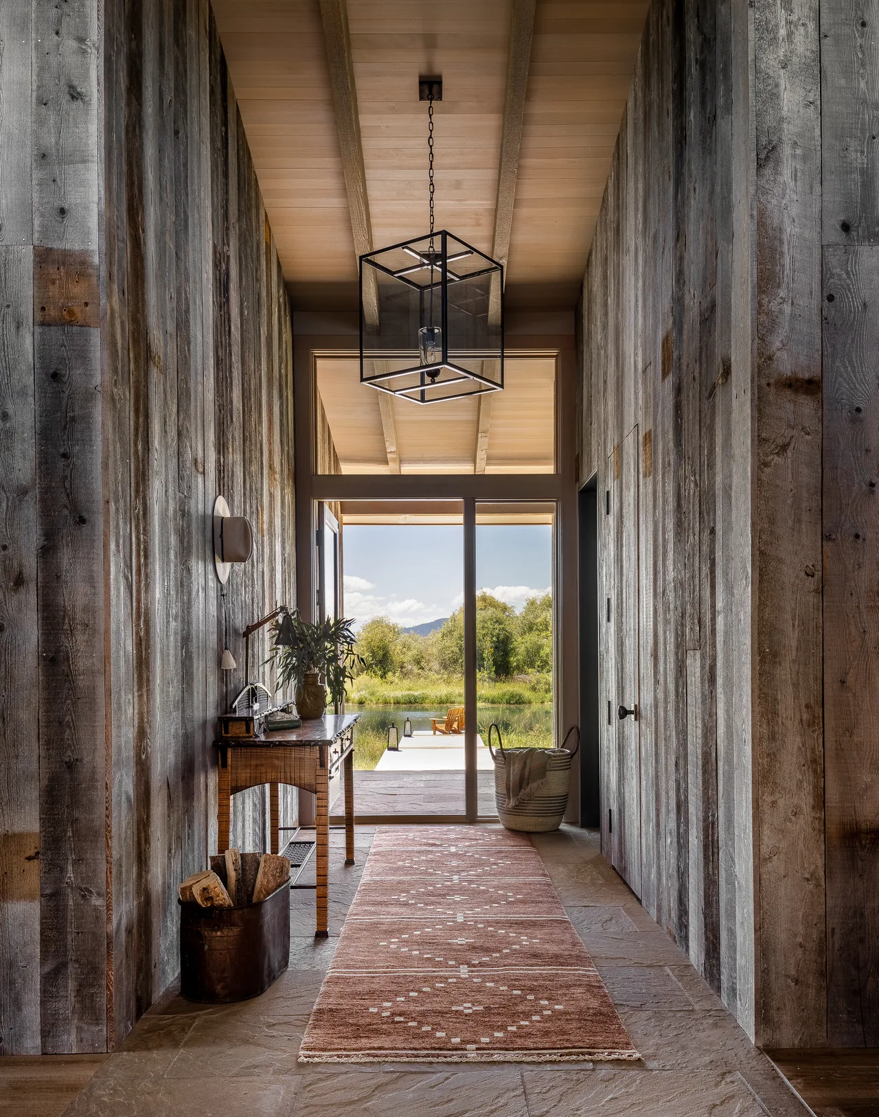 Hallway featuring weathered wood siding walls, stone floor, and a pendant light opening to an exterior view.