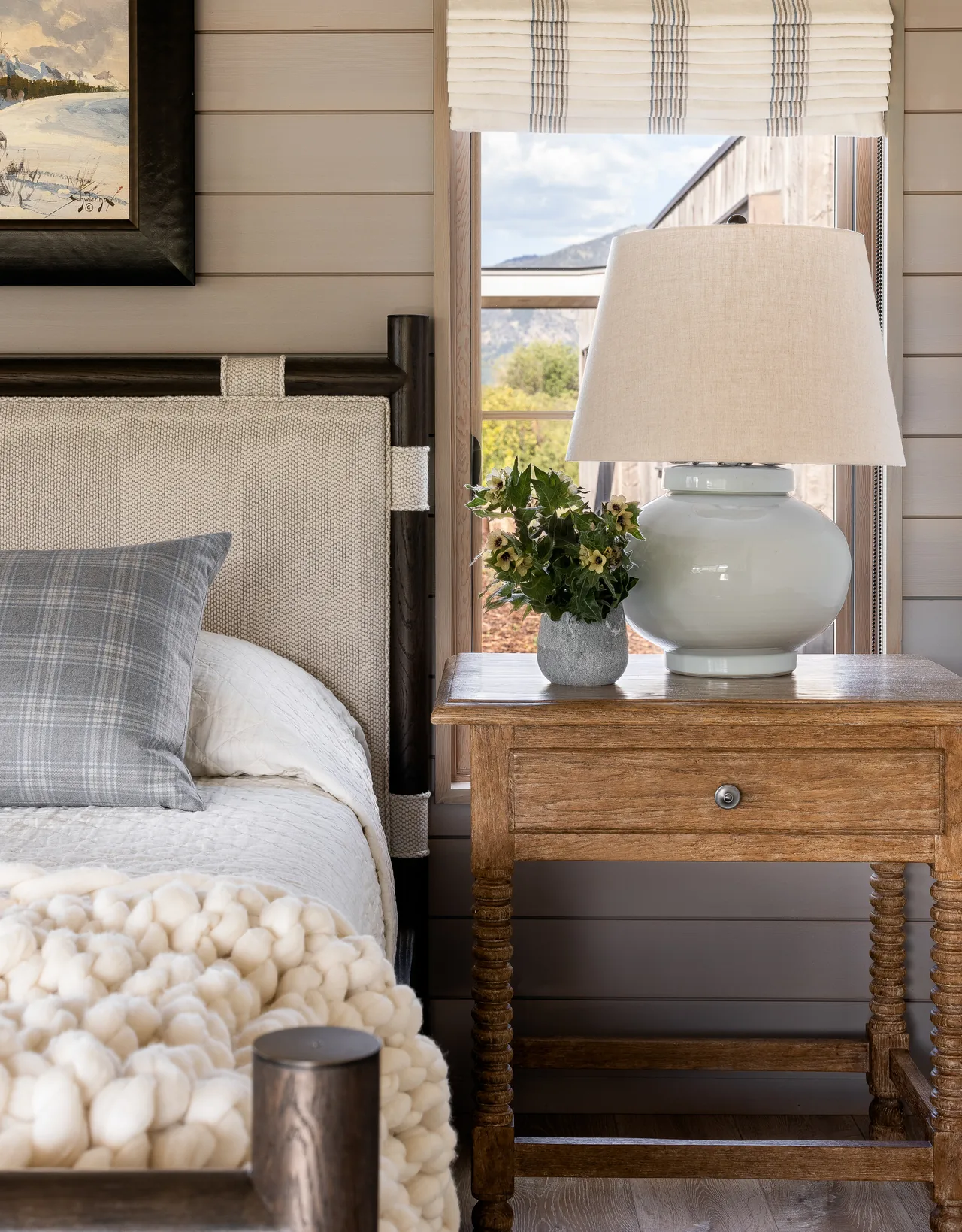 A cozy bedroom corner with a wood-framed upholstered bed, wooden nightstand, and soft lighting from a table lamp.
