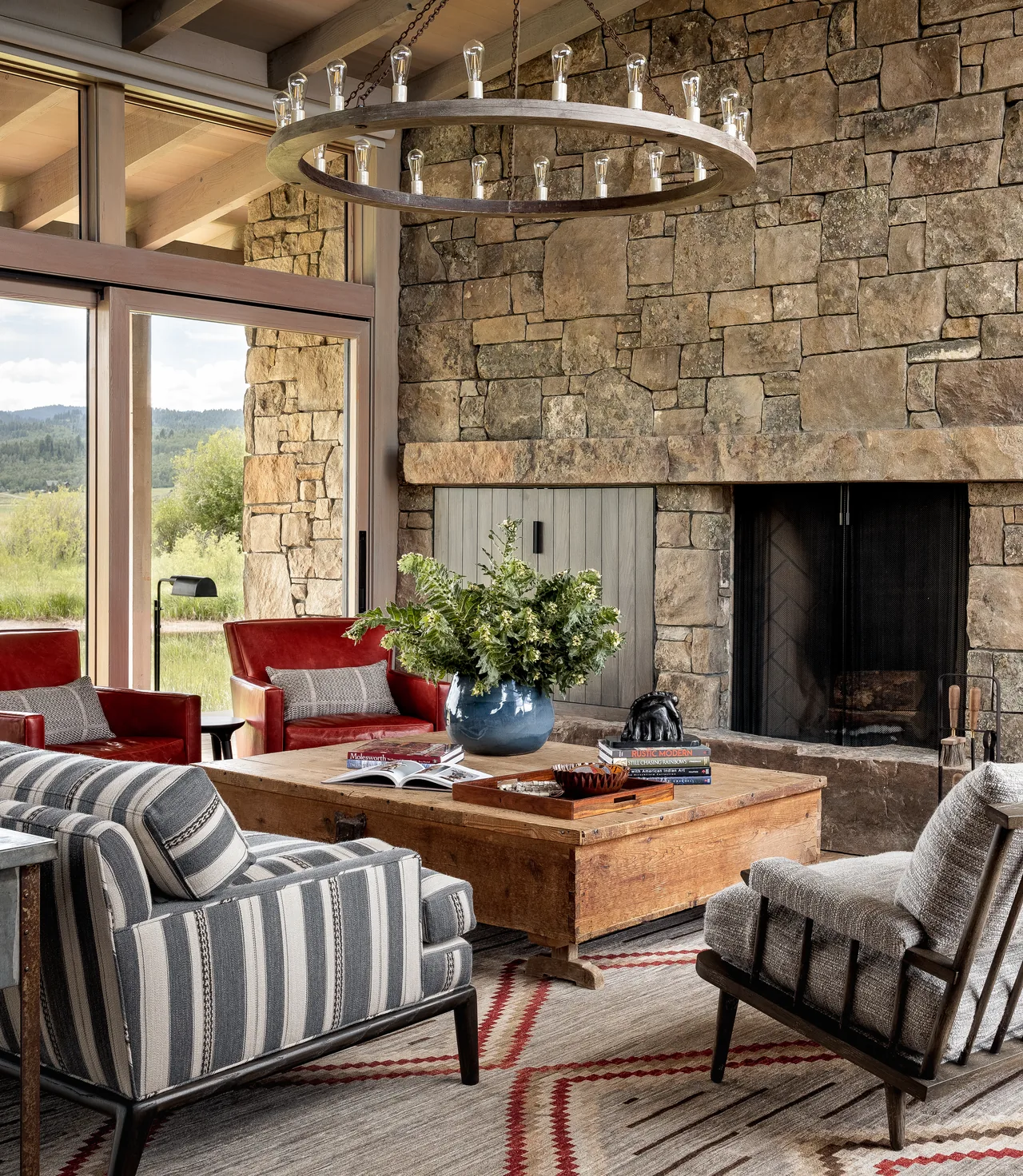 Cozy living room features a large stone fireplace surround, striped armchairs, and a wooden coffee table with a geometric rug.
