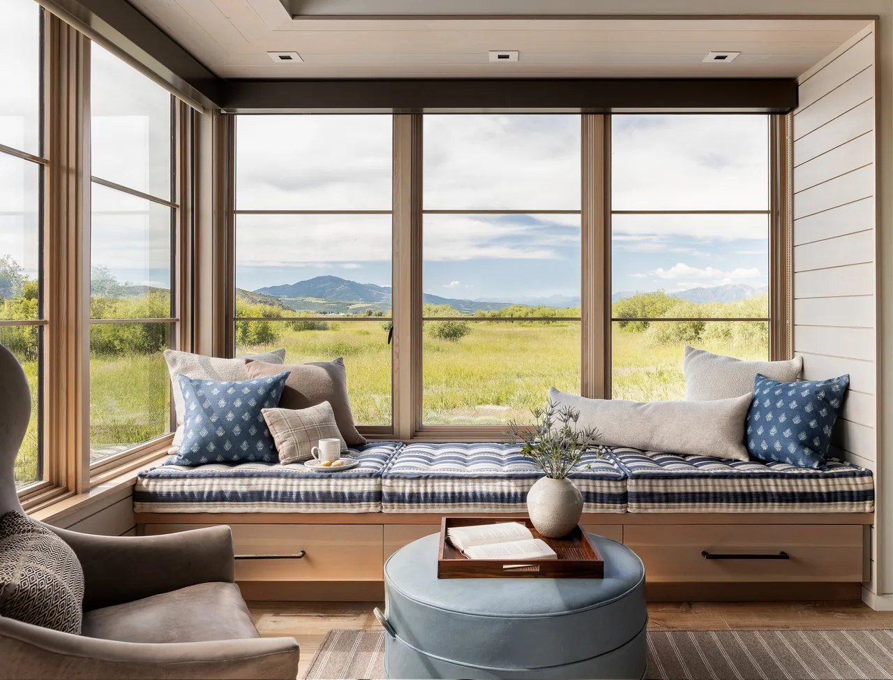 Window bench seating with cushions overlooks open landscape and mountains beyond.