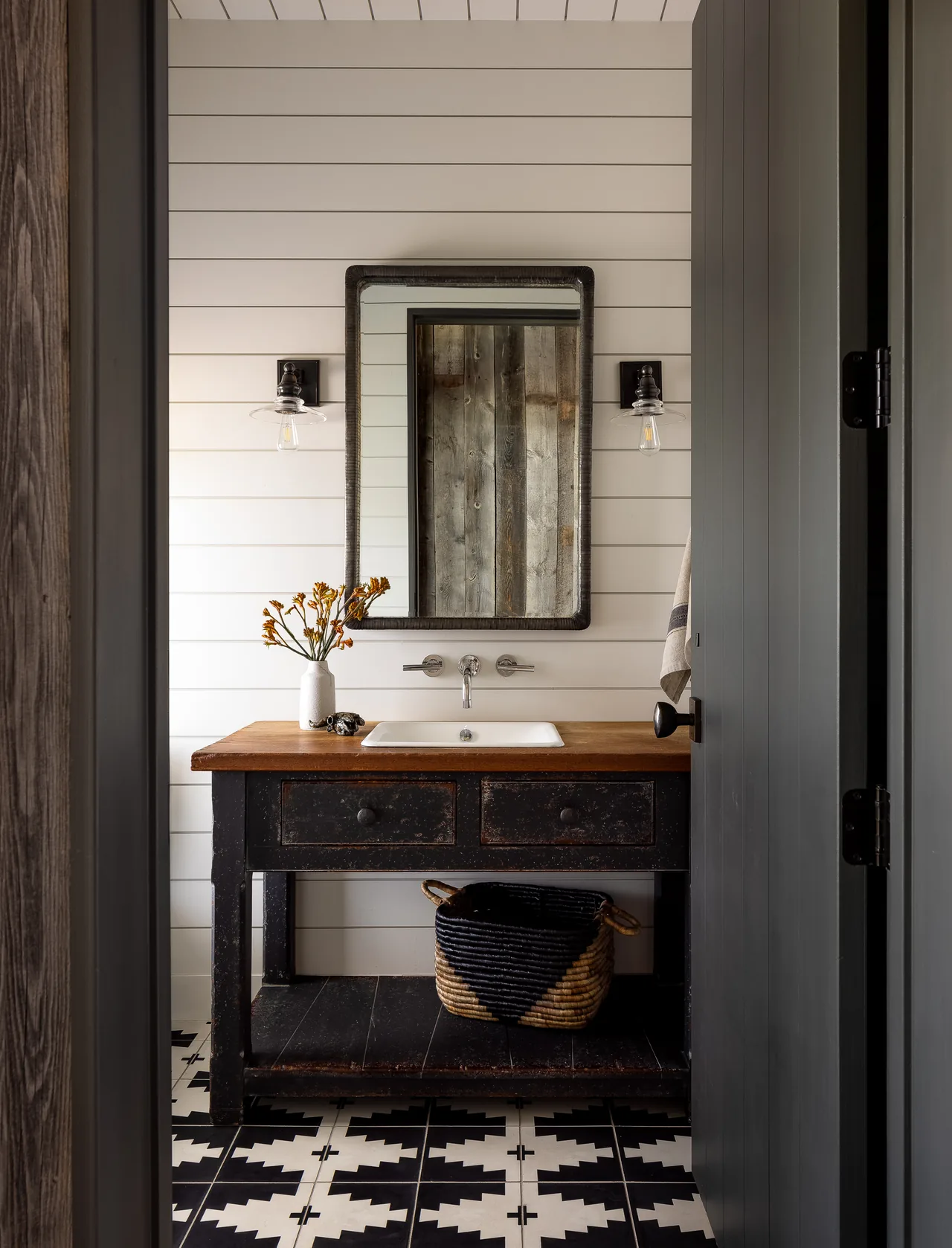 Bathroom vanity with a wooden countertop, wall-mounted faucet, and decorative lighting on shiplap walls.