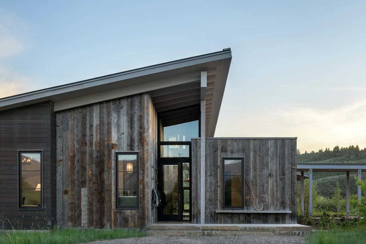 The Wyoming Retreat features weathered wood siding, a steep shed roof, and narrow vertical windows at the main entry.