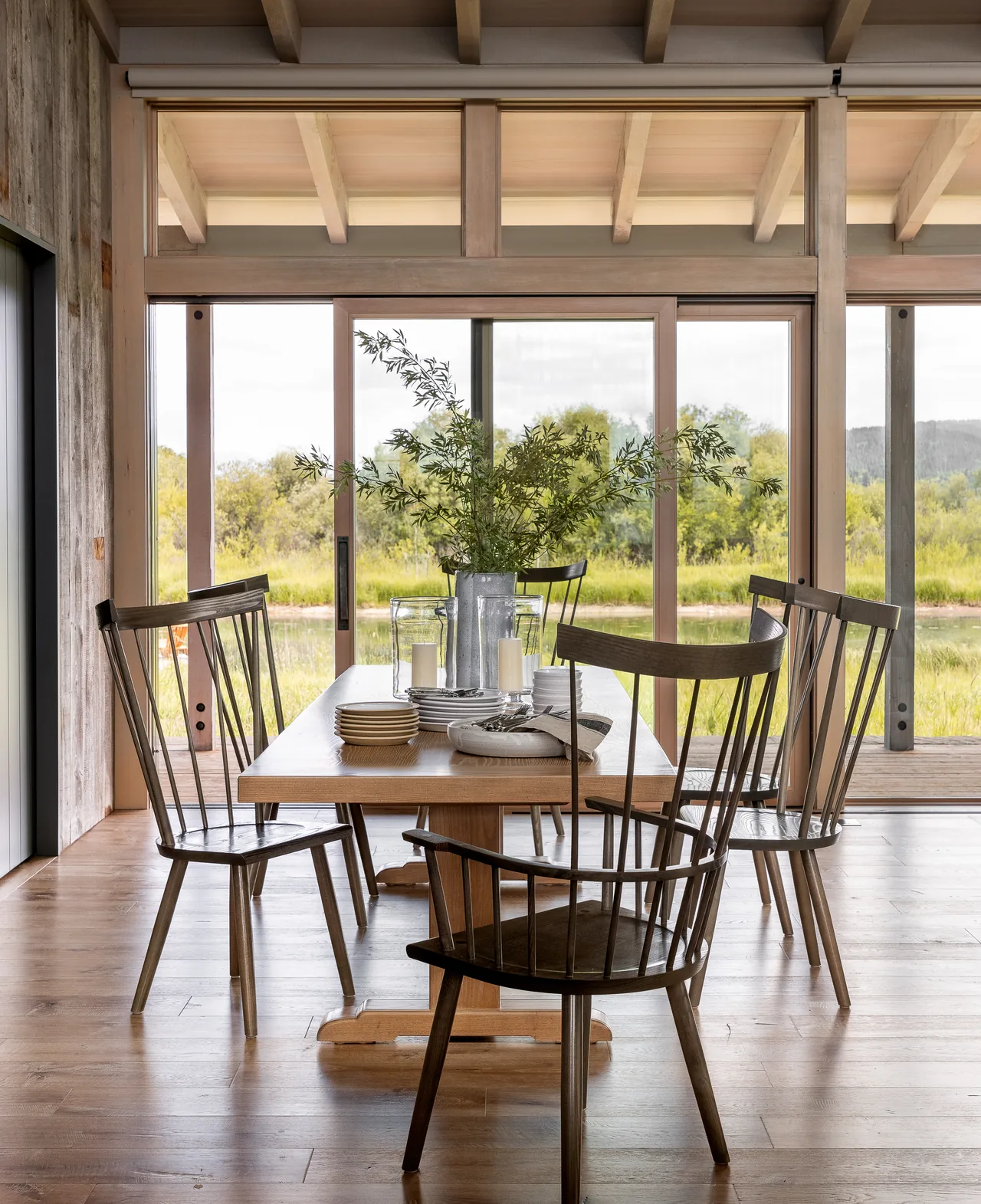 Dining area features wood table and chairs with large sliding glass doors opening to natural views.
