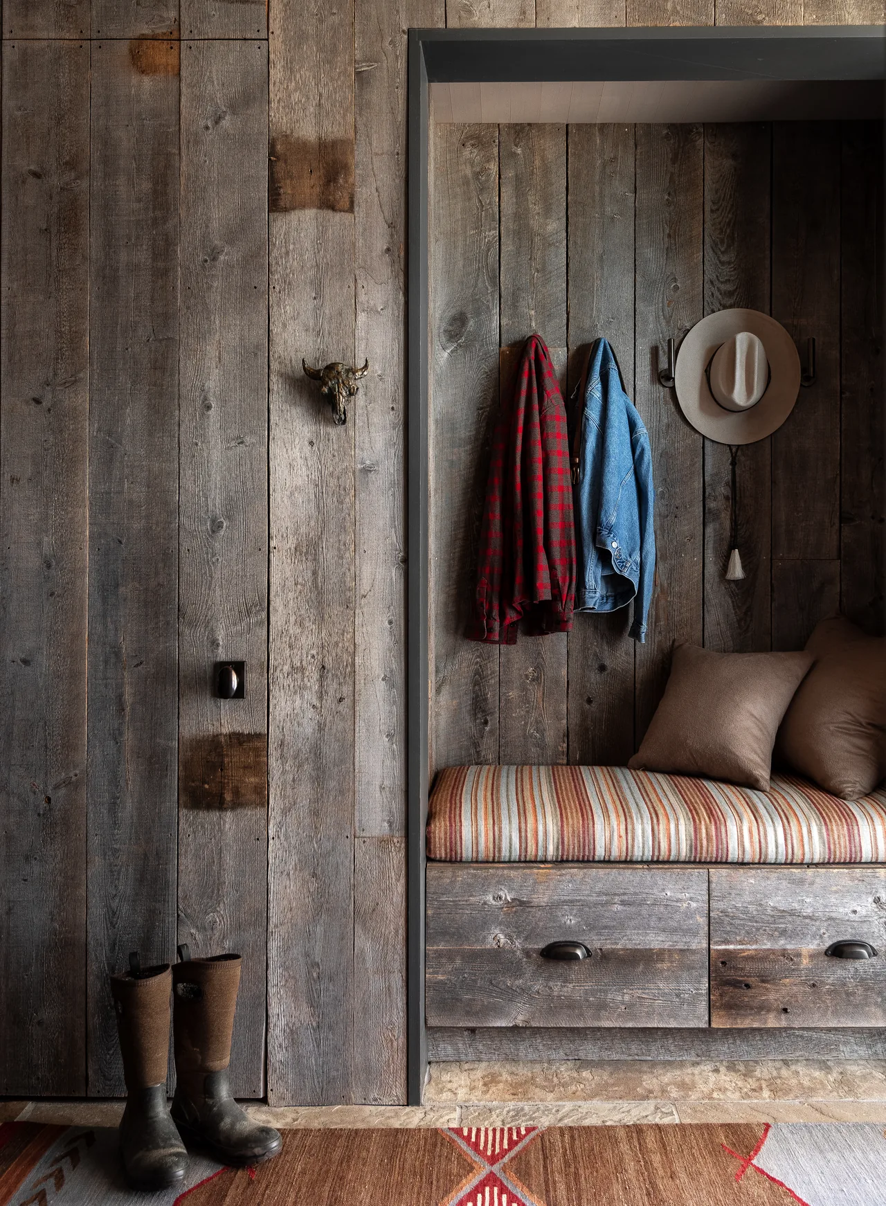 Entry space with weathered wood wall paneling, built-in bench seating, and hooks holding outerwear and a hat.
