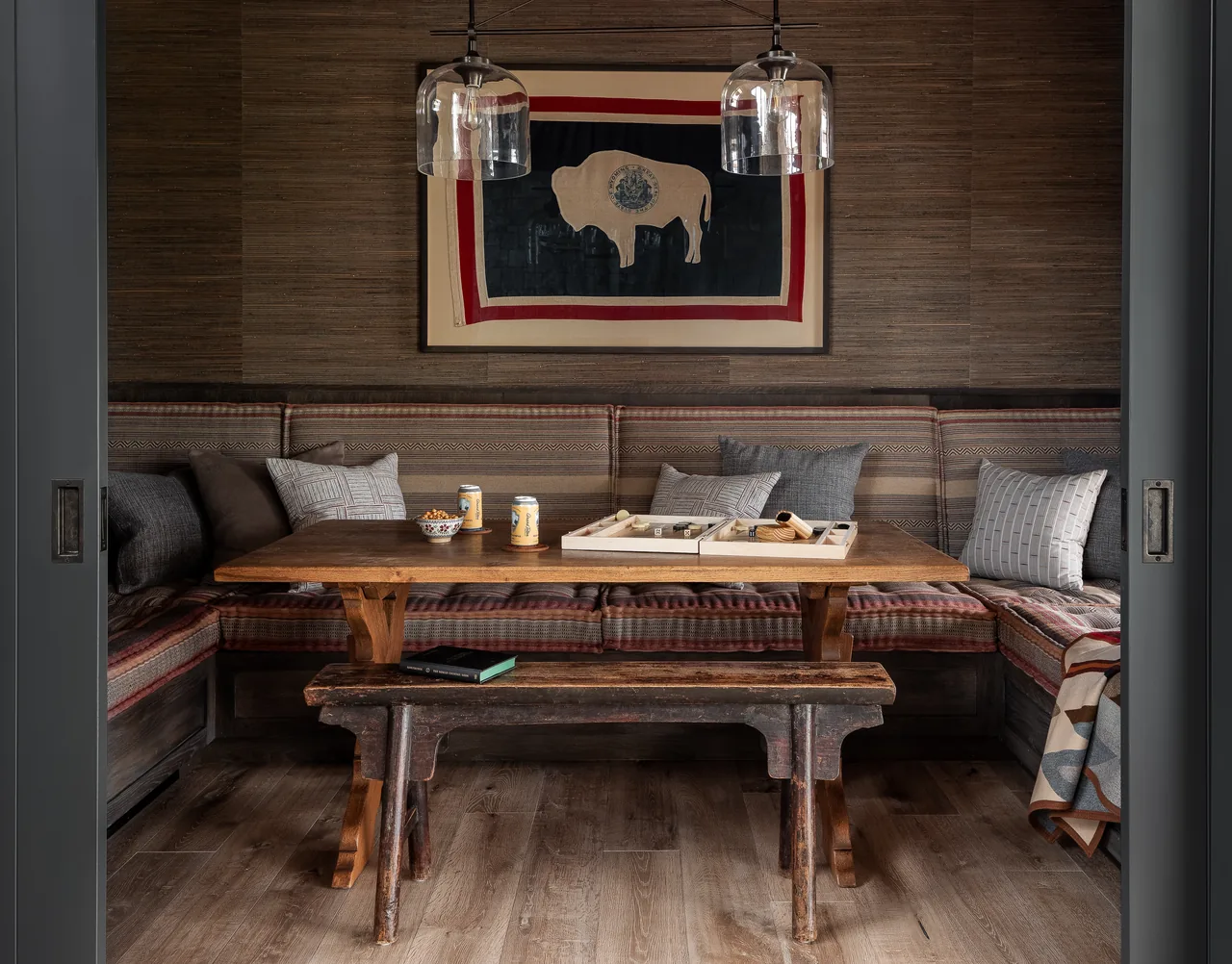 Dining nook features a wooden table with bench seating adorned by patterned cushions and a framed bison print on the wall.