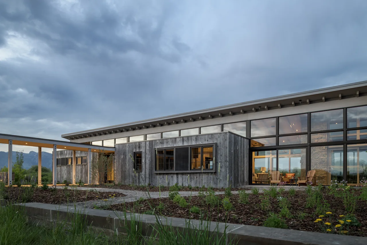 Wyoming Retreat features weathered wood siding and extensive glazing with a covered walkway under an angled roof.