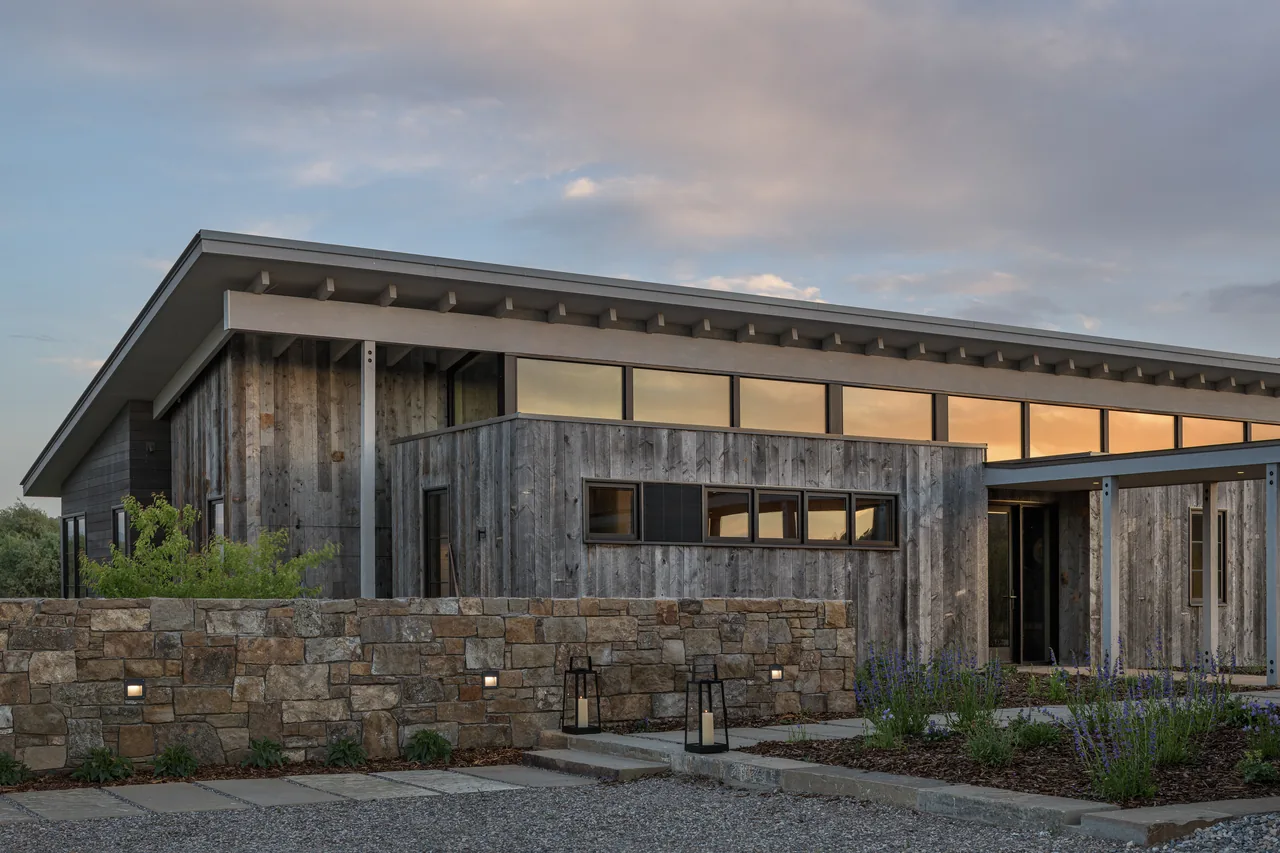 The Wyoming Retreat features weathered wood siding with a stone wall and a flat roof under glowing dusk skies.
