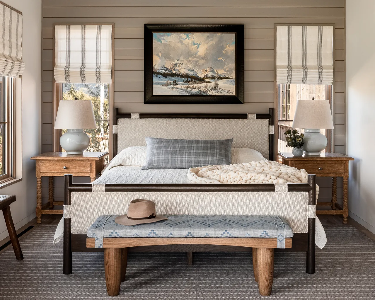 The Wyoming Retreat bedroom has a rustic contemporary style with upholstered bed, wooden furniture, and landscape artwork above the headboard.