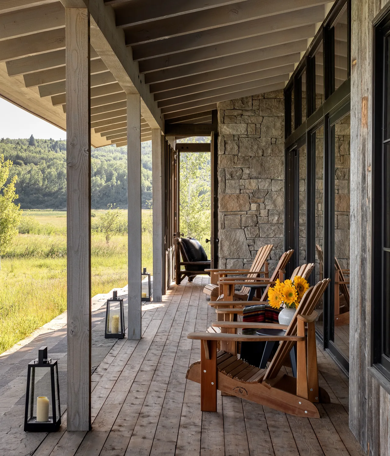 The Wyoming Retreat features a covered porch with Adirondack chairs and a stone exterior wall overlooking a natural landscape.
