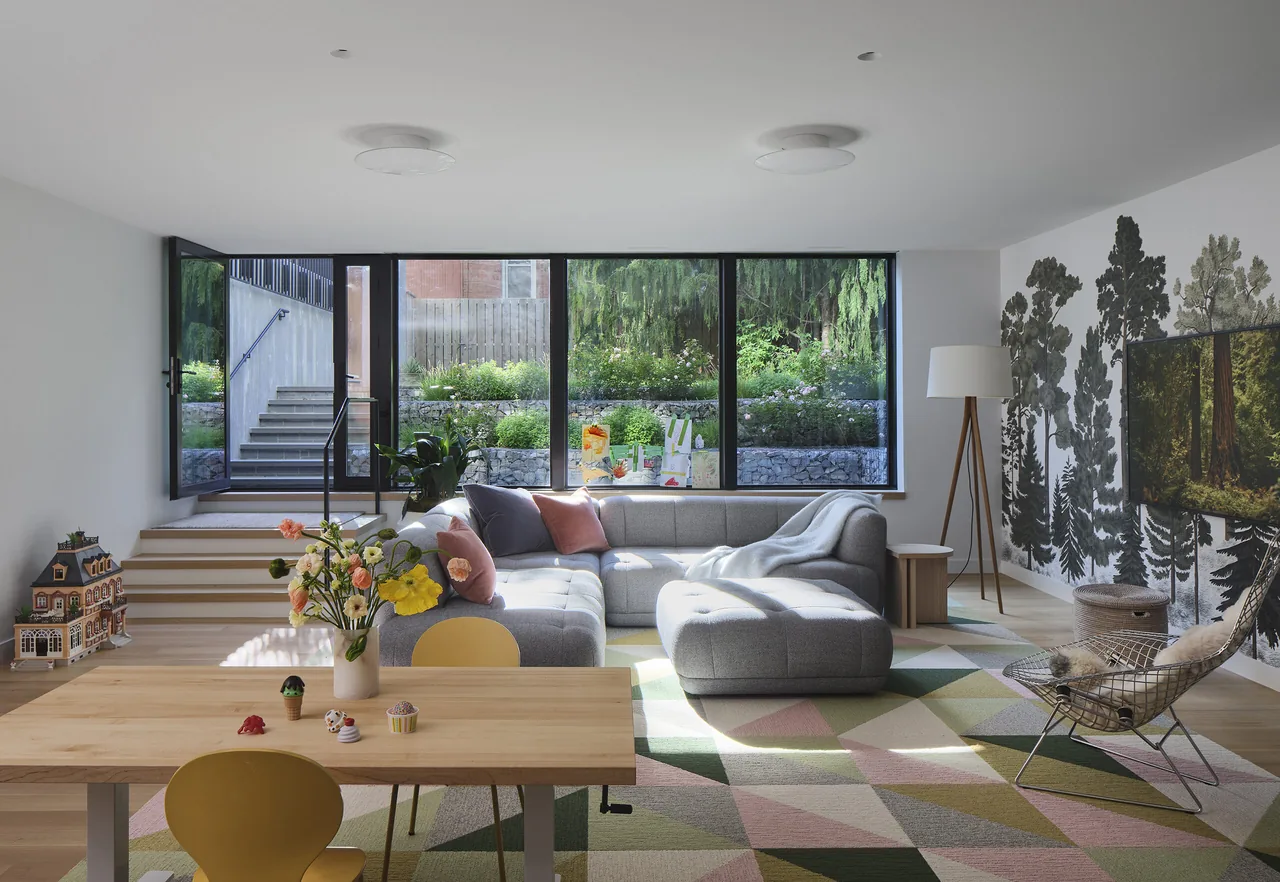 Living room featuring large black-framed windows looking out to a garden and a gray sectional sofa on a geometric rug.