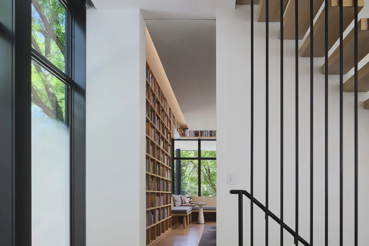 Interior residential library space with floor-to-ceiling bookshelf and large windows.