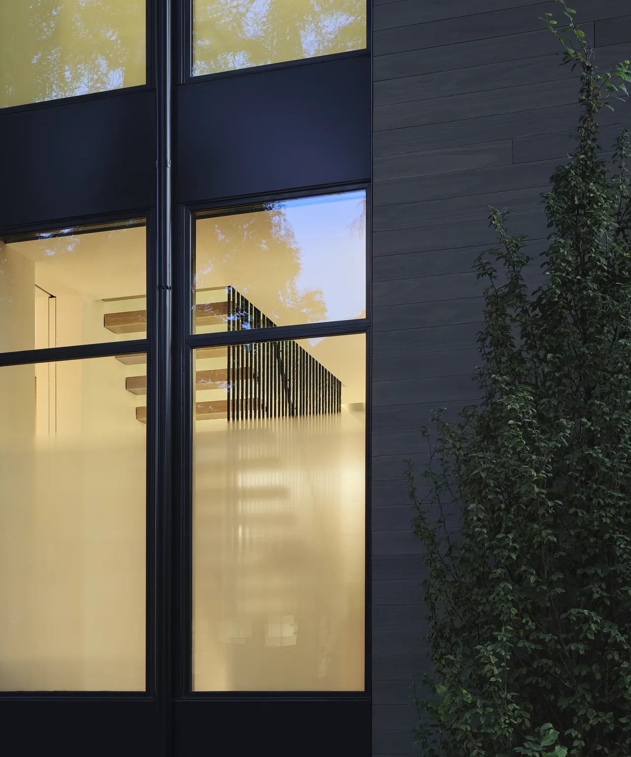 Modern exterior window detail with black frames and mixed frosted and clear glass, revealing an interior staircase with wood steps.