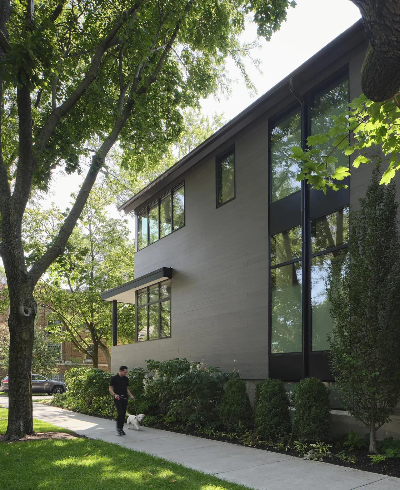 Side exterior view of the Lakewood Balmoral Residence showing wood siding and large black-framed windows.