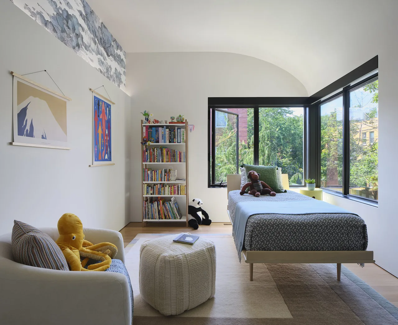 A bedroom with corner floor-to-ceiling windows, a single bed, bookshelves, and varied decorative elements.