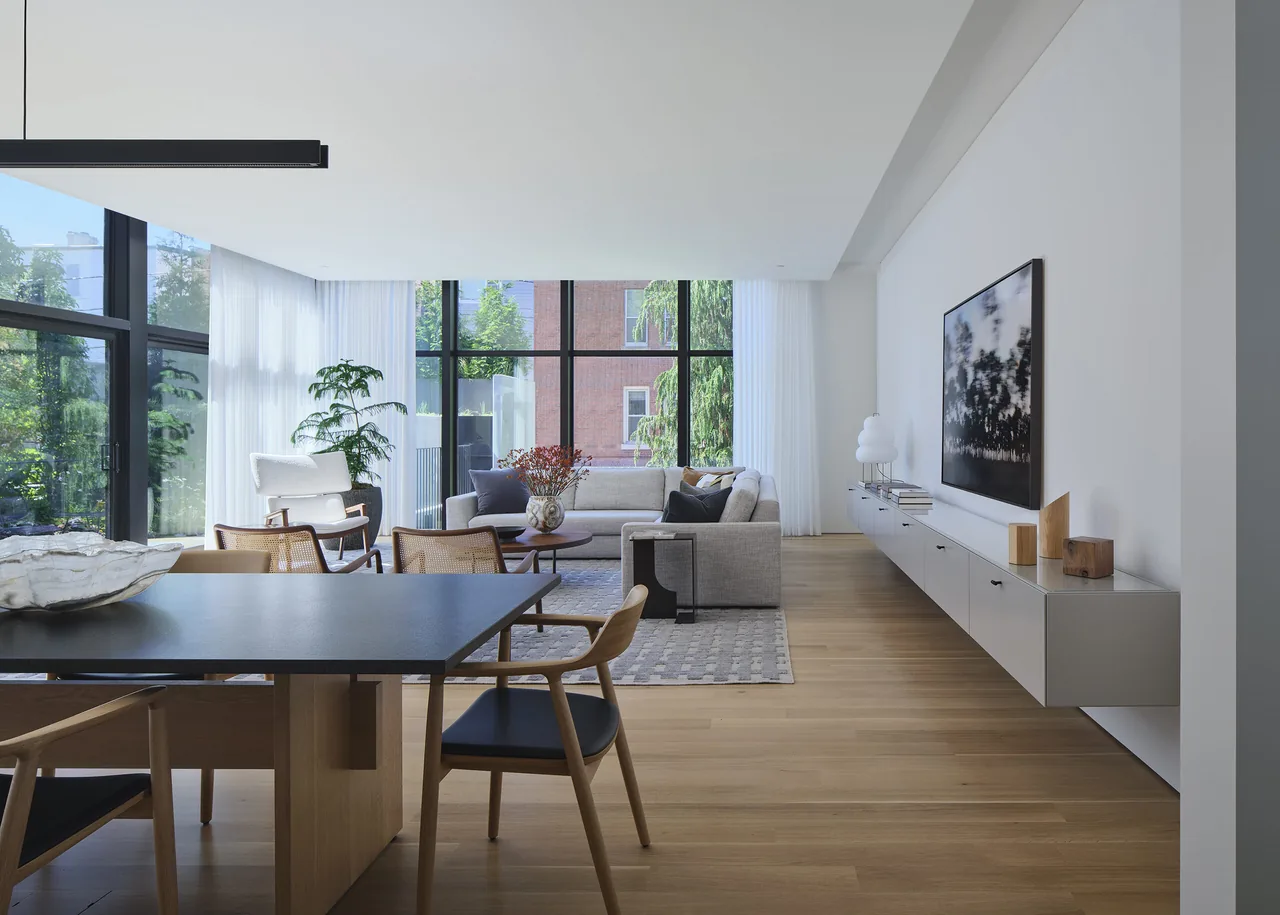 Living room and dining room with floor-to-ceiling glazing and light wood flooring.