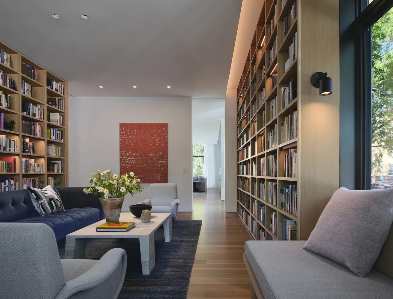 Living room interior features built-in bookshelves, a navy-blue sofa, armchairs, and a marble coffee table on a blue rug.