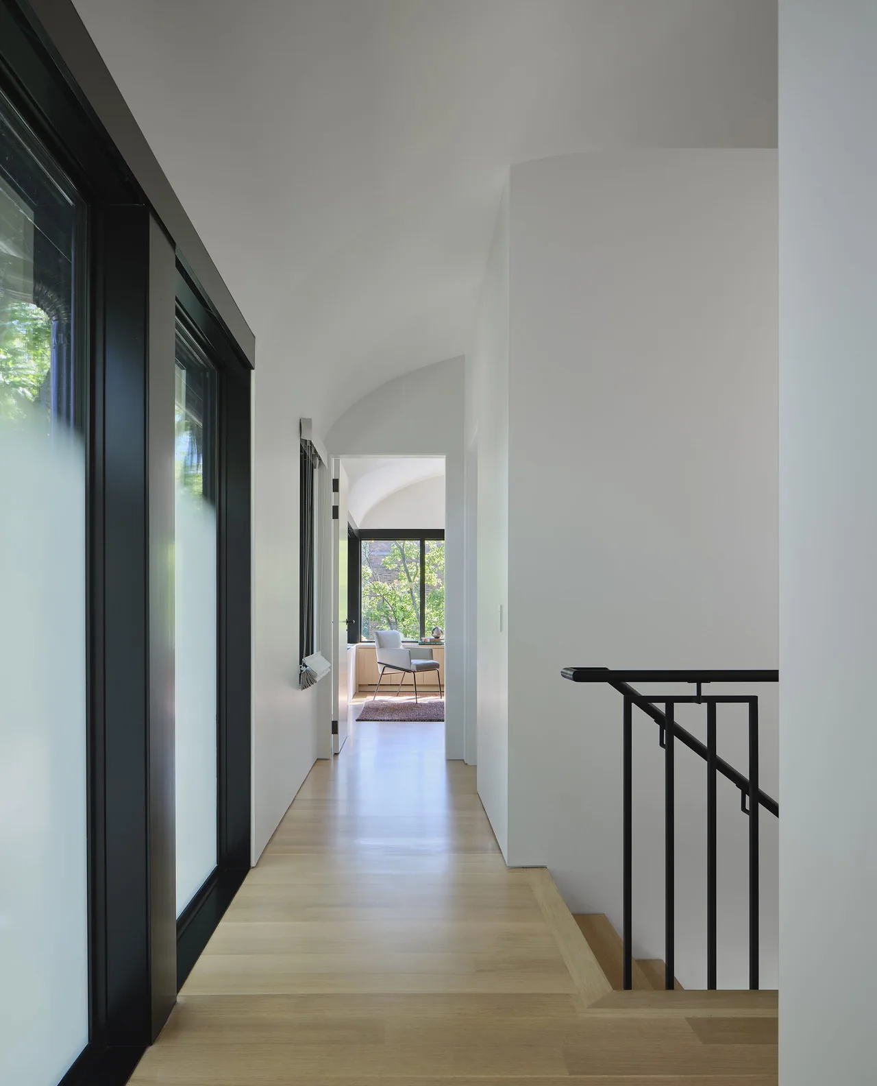 Hallway in Lakewood Balmoral Residence features light wood floors, white curved ceilings, and black trim around windows and stair railing.