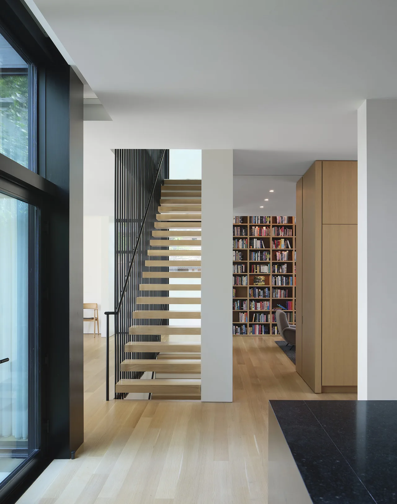 Floating wooden staircase with vertical metal railings adjacent to a built-in wooden bookshelf in a residential interior.