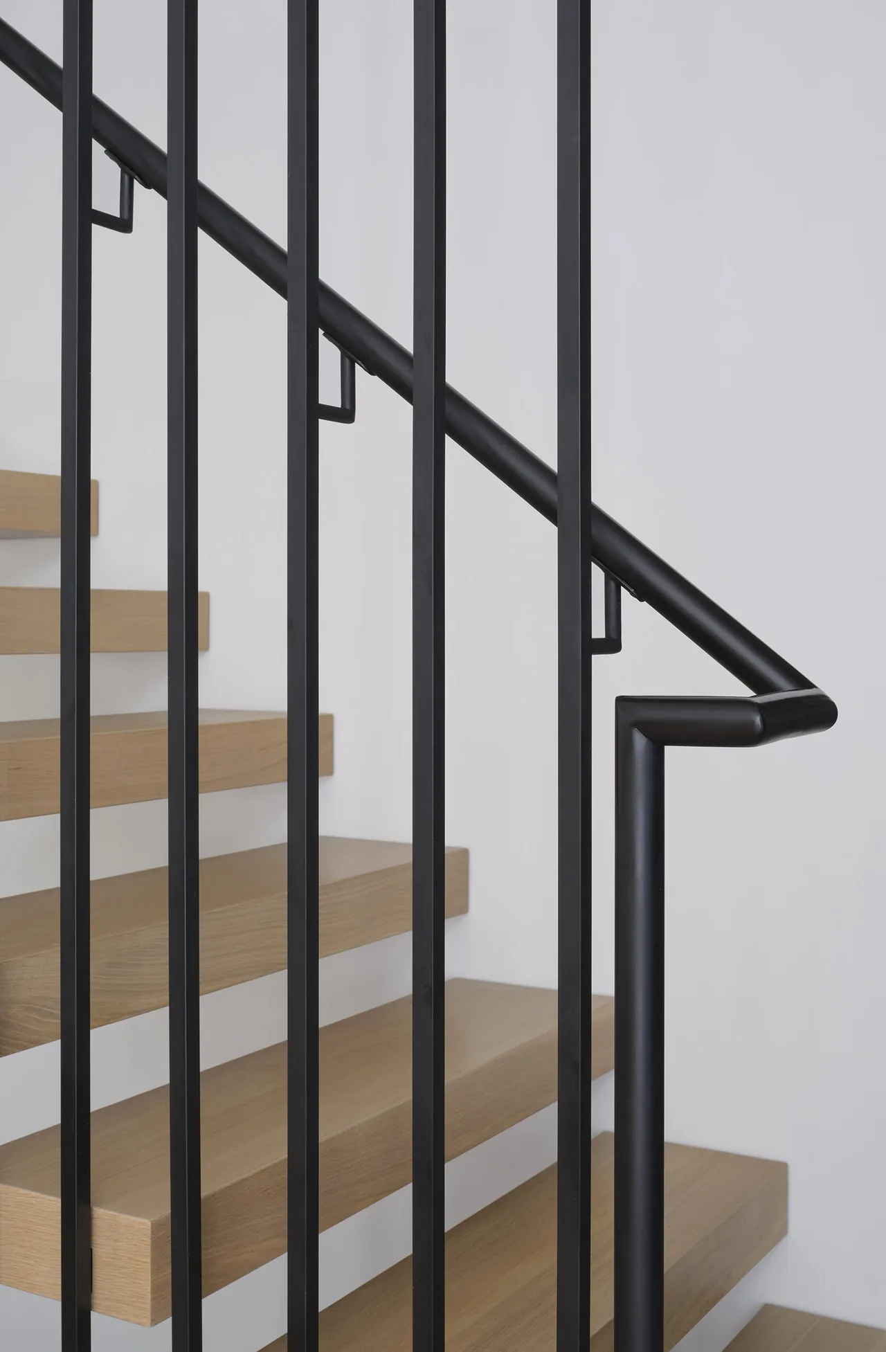 Detail of a staircase showing black metal vertical balusters and wooden floating treads.