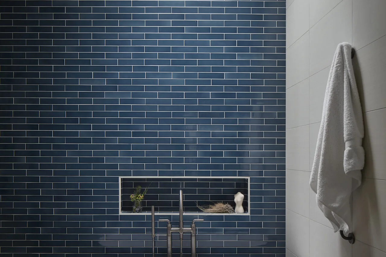 Bathroom wall featuring dark blue subway tiles with a rectangular recessed niche beside white tiled wall with towel hook.
